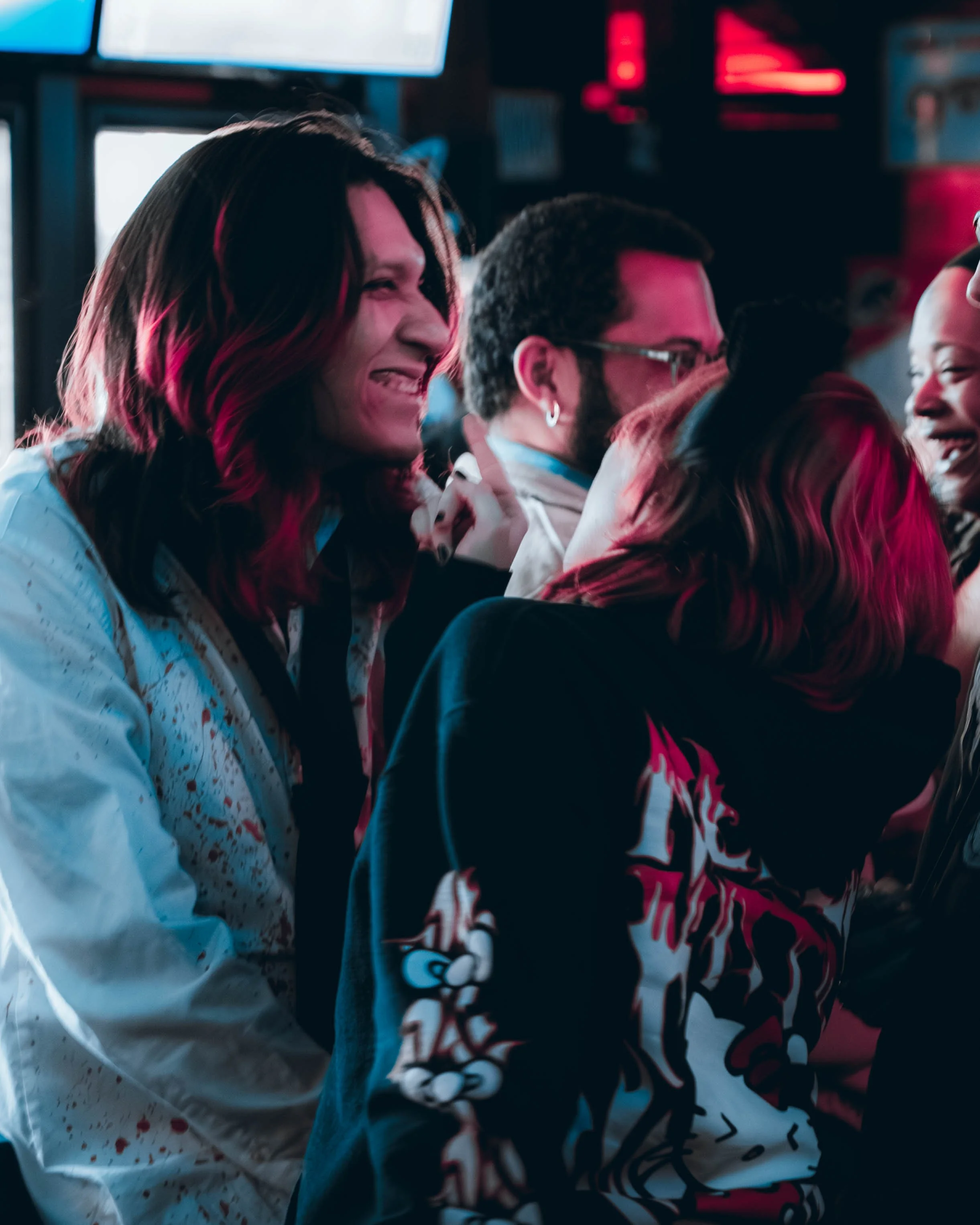 Four friends or colleagues smiling and laughing together at a social gathering or party, illuminated by colorful lighting.