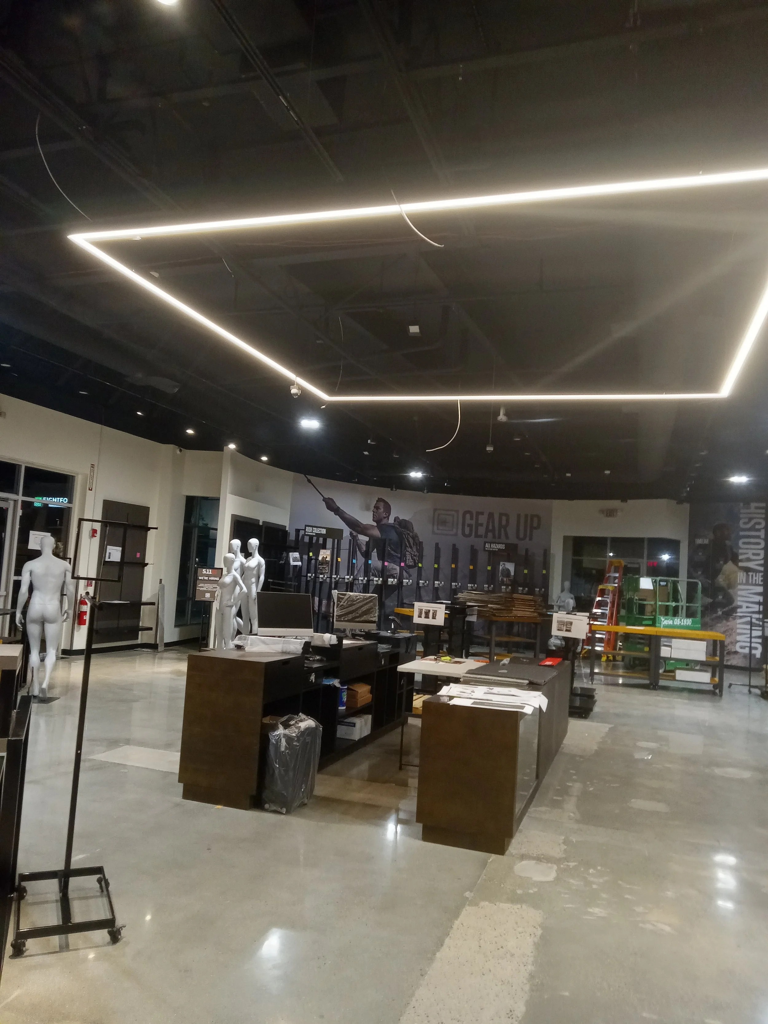 Empty retail store or showroom with mannequins, display tables, and shelves, under modern lighting fixtures.
