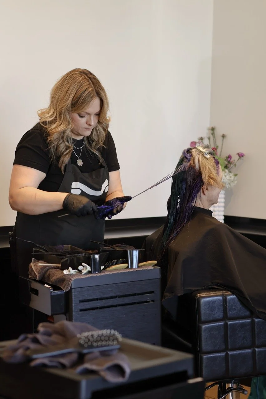 A woman with blonde hair getting her hair dyed by a hairstylist in a salon.