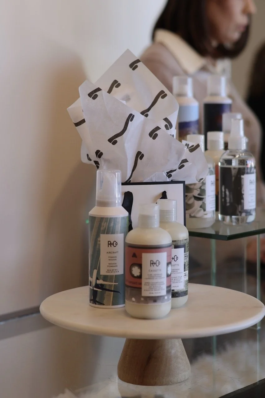 Display of various toiletries including bottles of soap, lotion, and other personal care products on a small round table with tissue paper in the background.