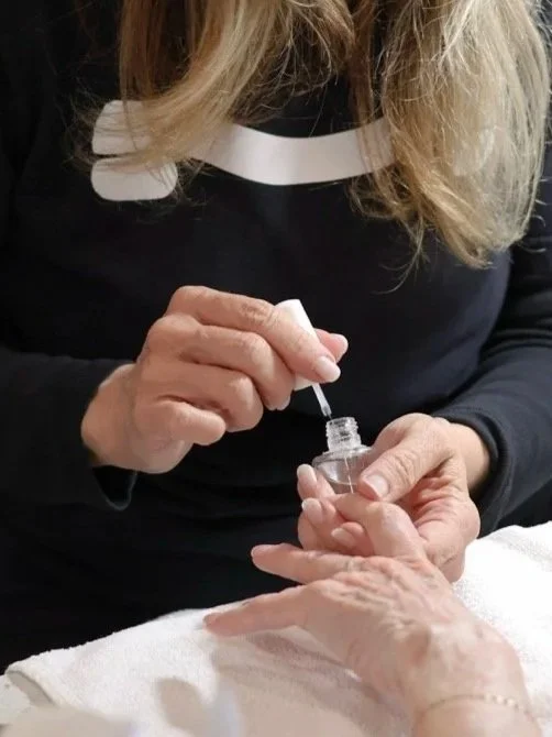 A woman is applying clear nail polish to an elderly person's fingernails.