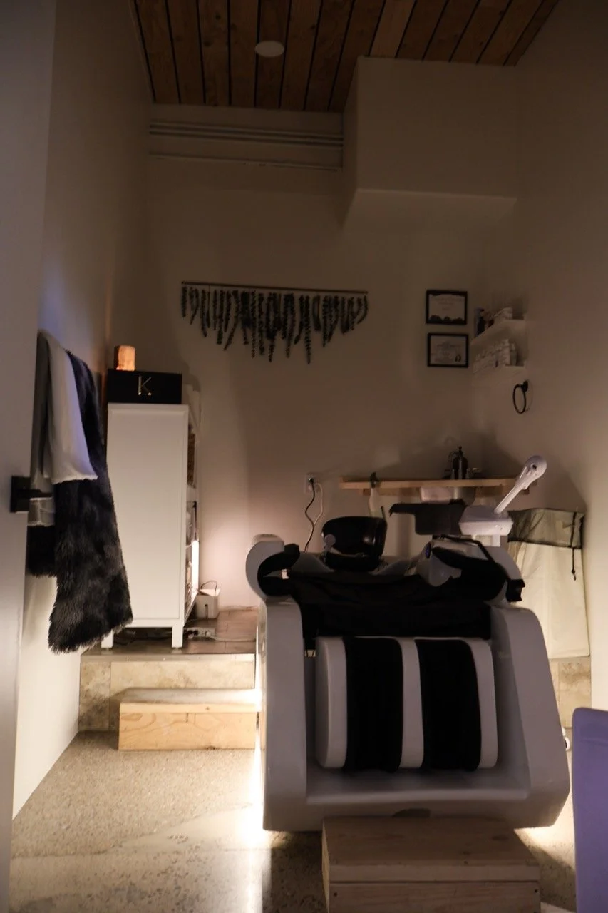 A massage or therapy room with a massage chair, a small cabinet, and framed certificates on the wall.
