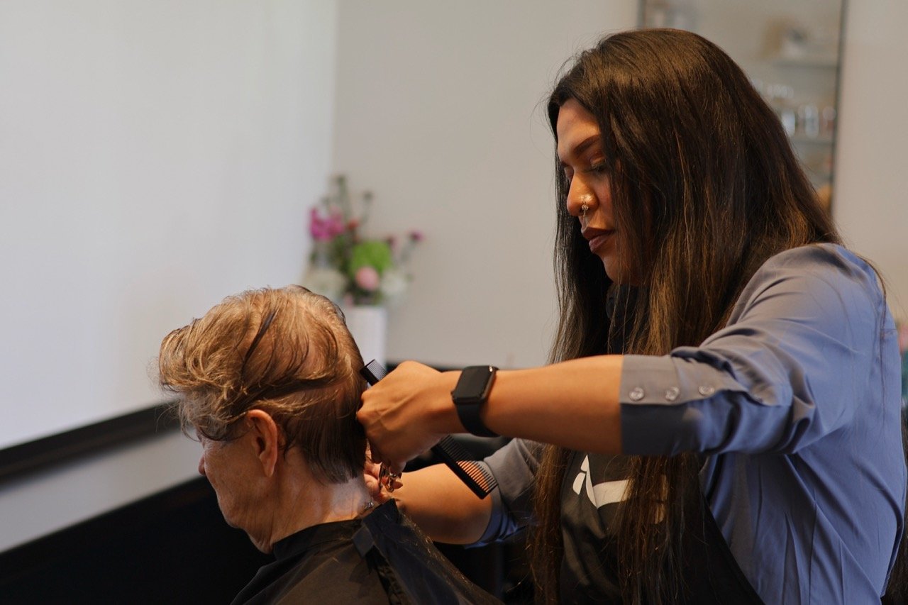 A hairstylist cutting an elderly woman's hair in a salon.