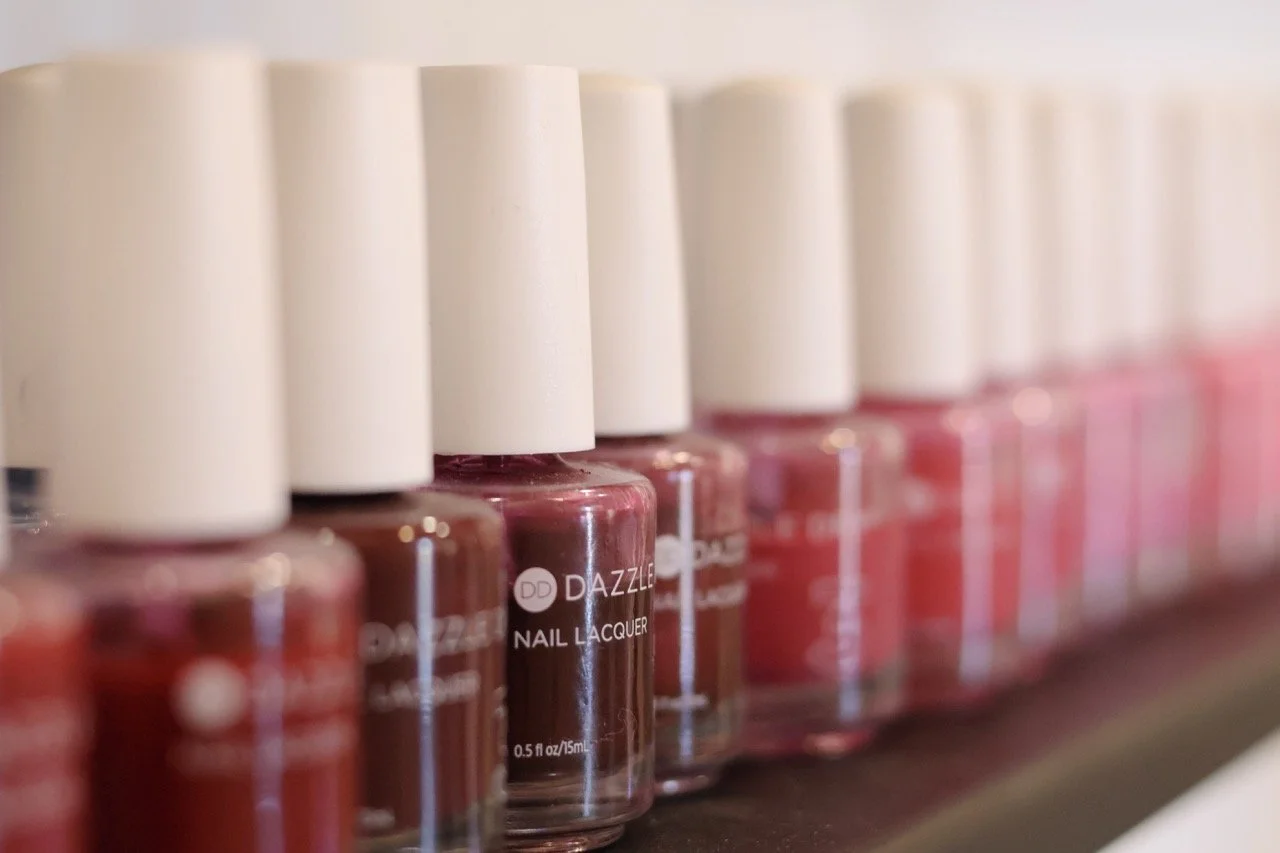 A row of pink and red nail polish bottles on a shelf, with white caps, captured in a close-up shot.