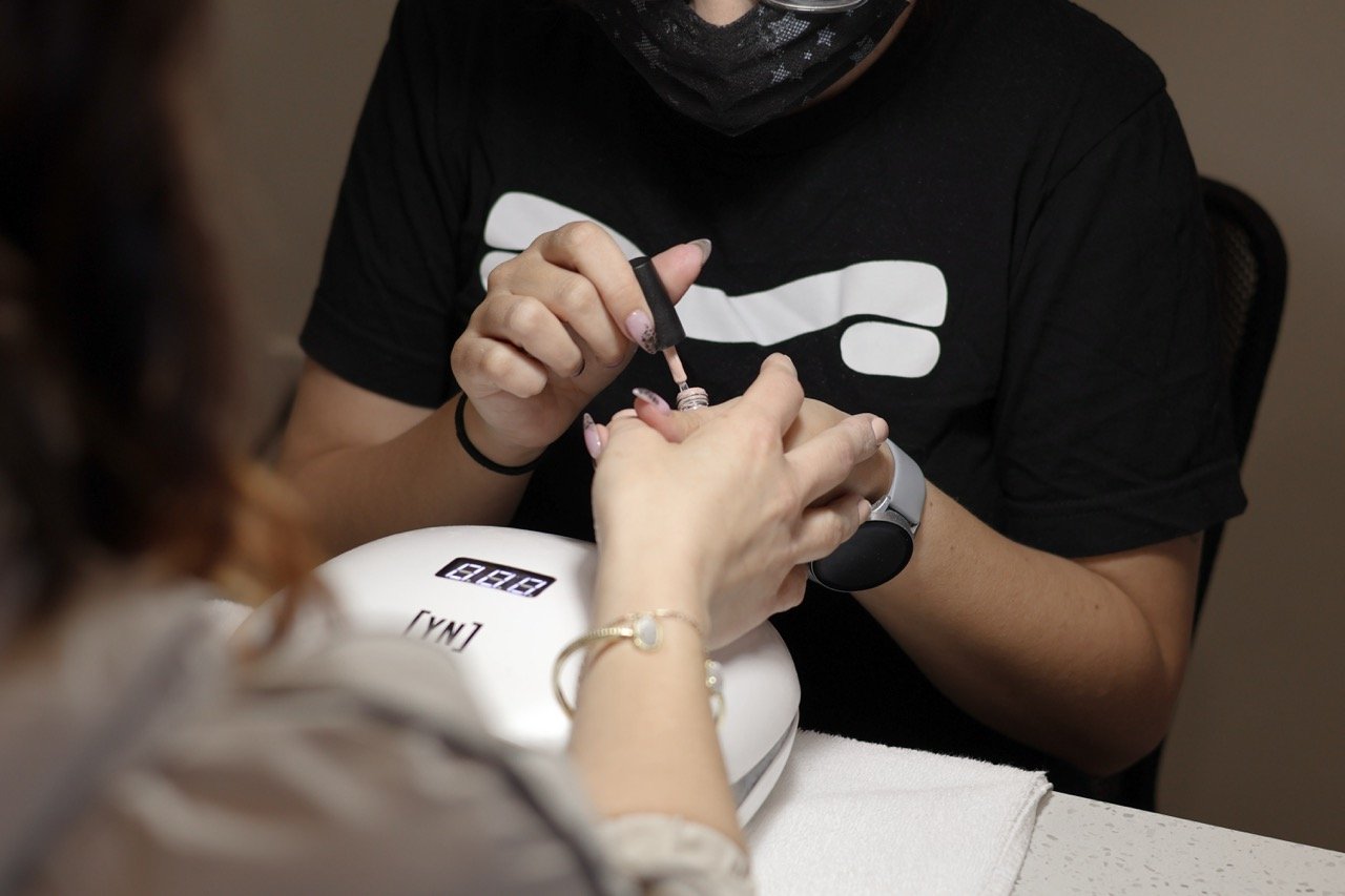 Manicurist applying nail polish to a client's fingernails in a nail salon.