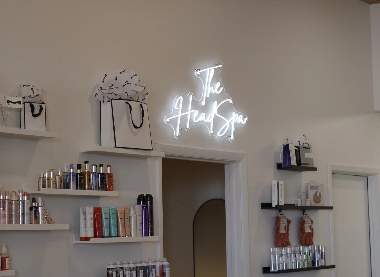 Interior wall of The Head Spa with shelves of hair care products, gift bags, and a neon sign reading 'The Head Spa'