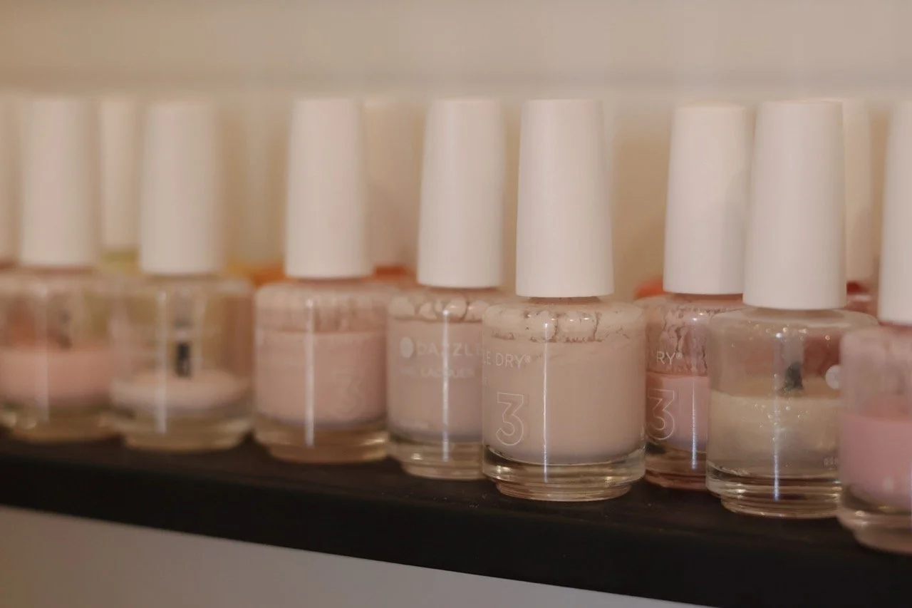 Several bottles of light pink nail polish lined up on a black surface.
