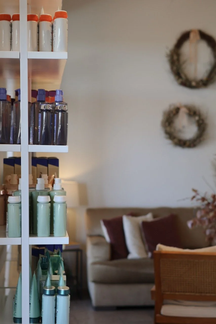 Shelves filled with various bottles and containers, with a living room in the background that includes a sofa with pillows, a wooden chair, and wall decorations.