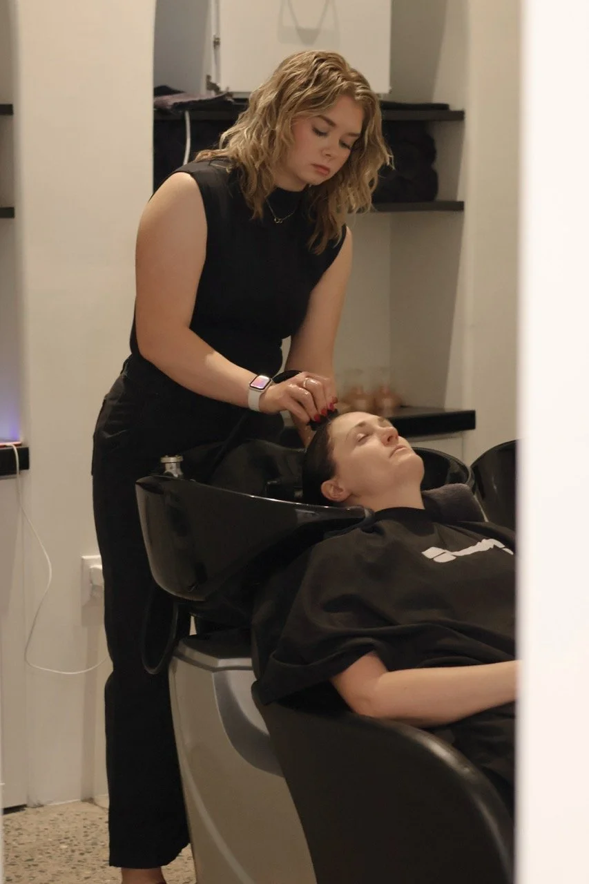 A woman getting her hair washed at a salon or hair salon, with her eyes closed and a woman standing behind her, washing her hair.