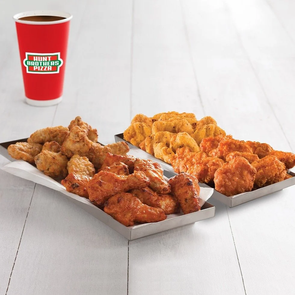 Three trays of fried chicken pieces with different coatings, a cup of soda on a white table.