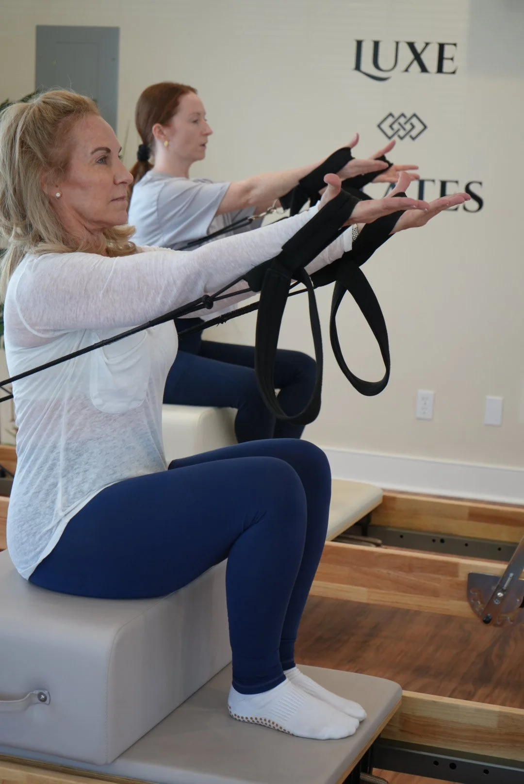 Two women doing Pilates exercises on reformer machines in a fitness studio.
