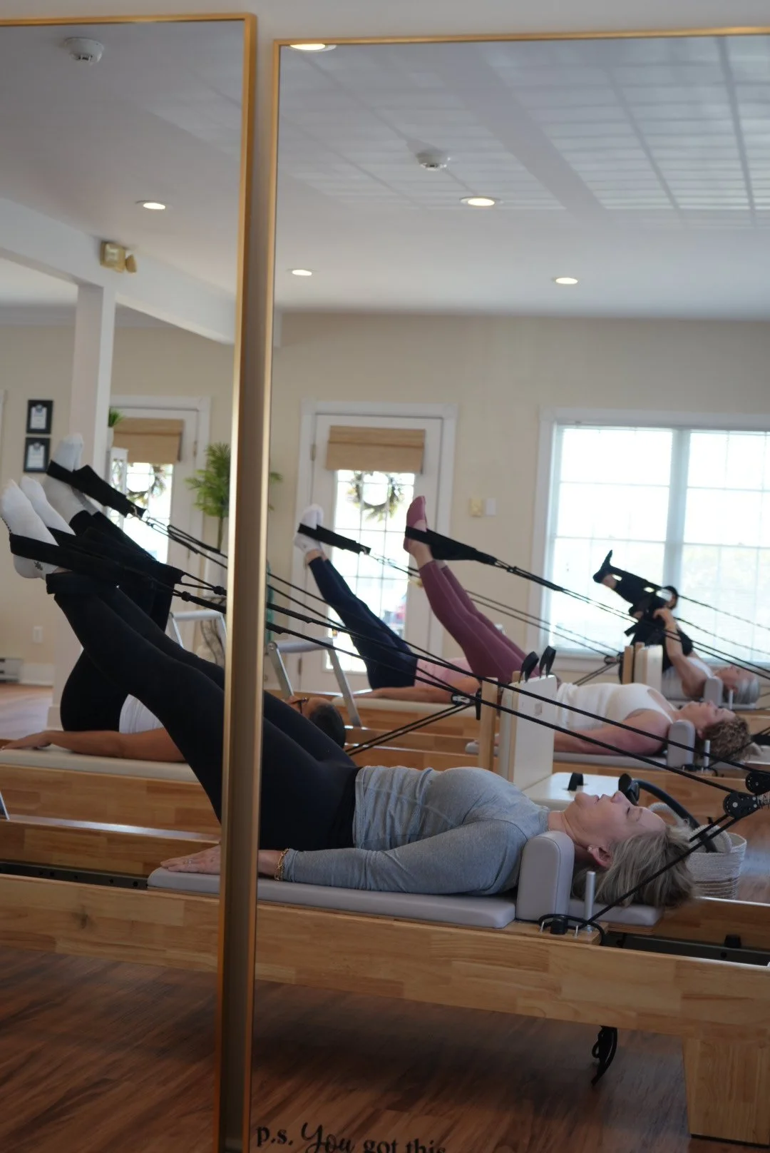 Women exercising with resistance bands attached to reformer beds in a Pilates studio.