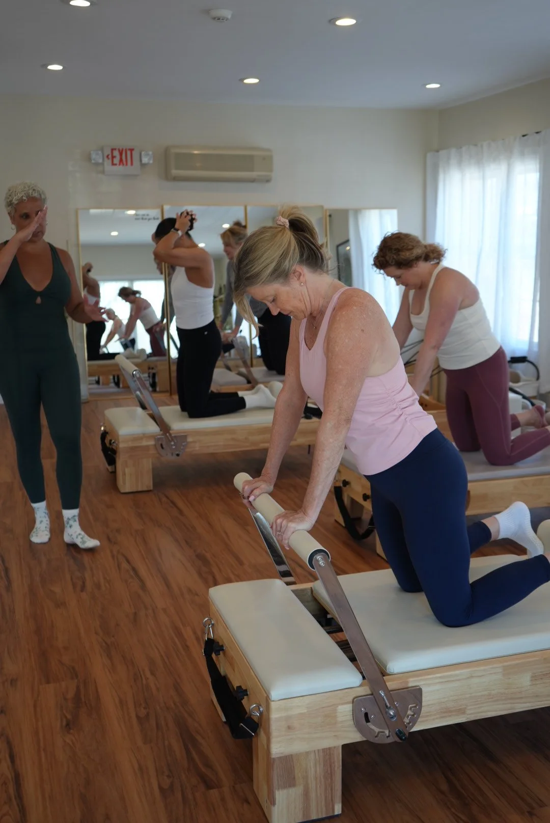Group of women doing Pilates exercises on reformer machines in a bright studio.