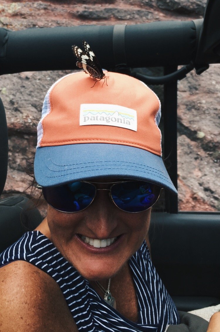 A professional organizer wearing a Patagonia cap and sunglasses, smiling with a butterfly resting on her cap.