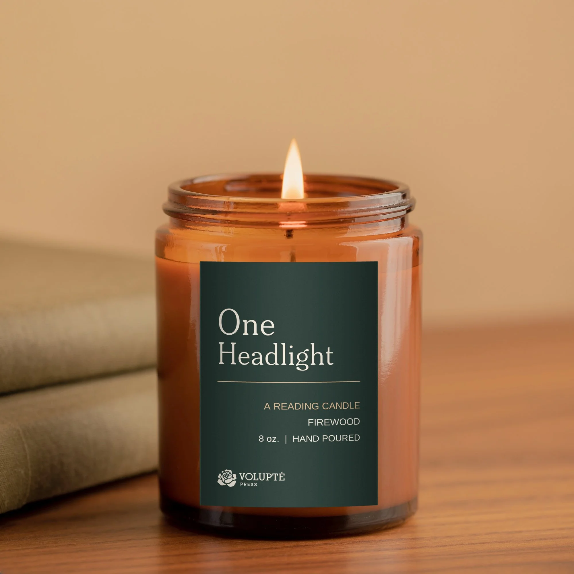 The One Headlight Reading Candle, a lit firewood-scented candle in an amber glass jar with a dark green Volupté Press label