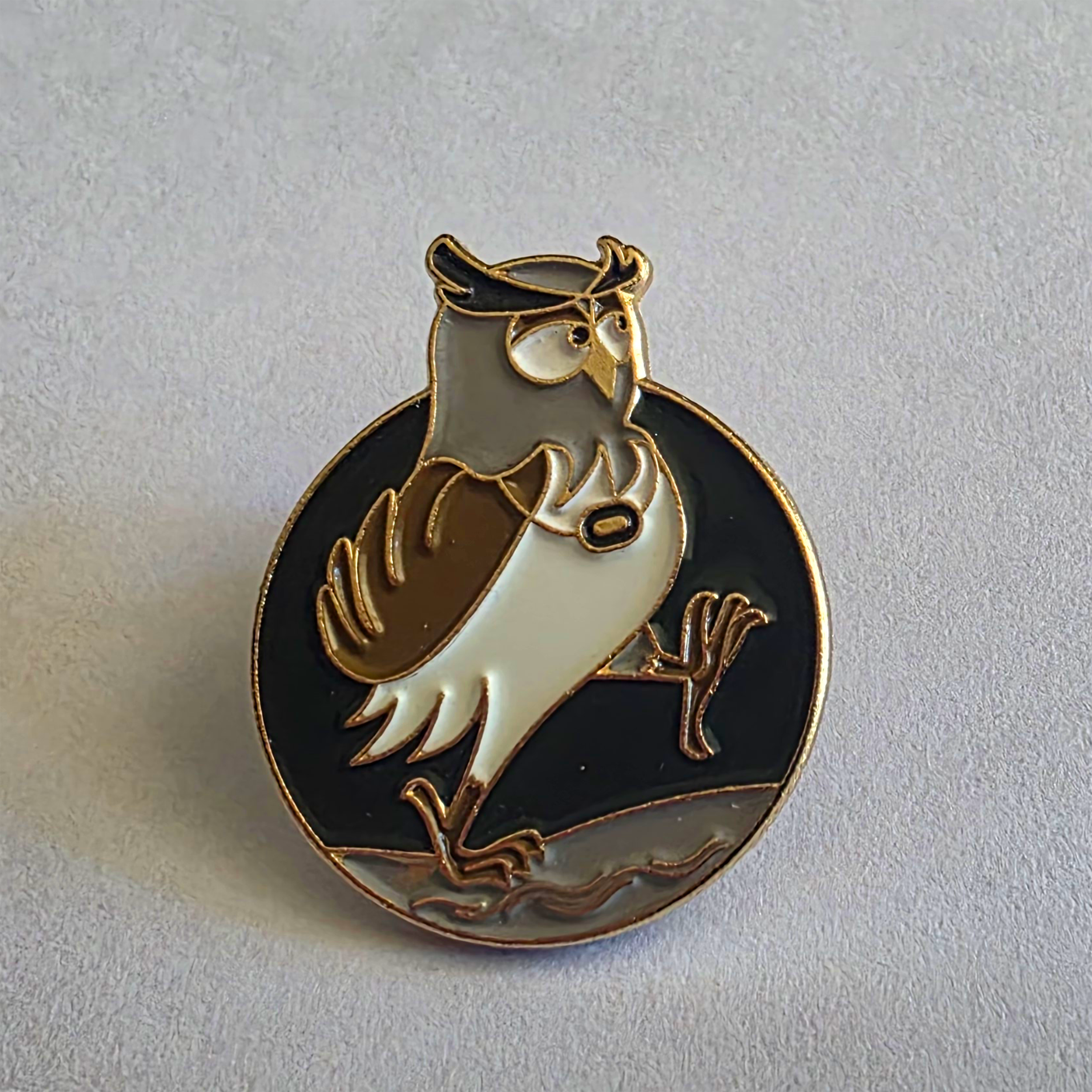 A decorative pin featuring an owl wearing glasses and a hat, holding a coffee mug, with a black and white background inside a circular frame.