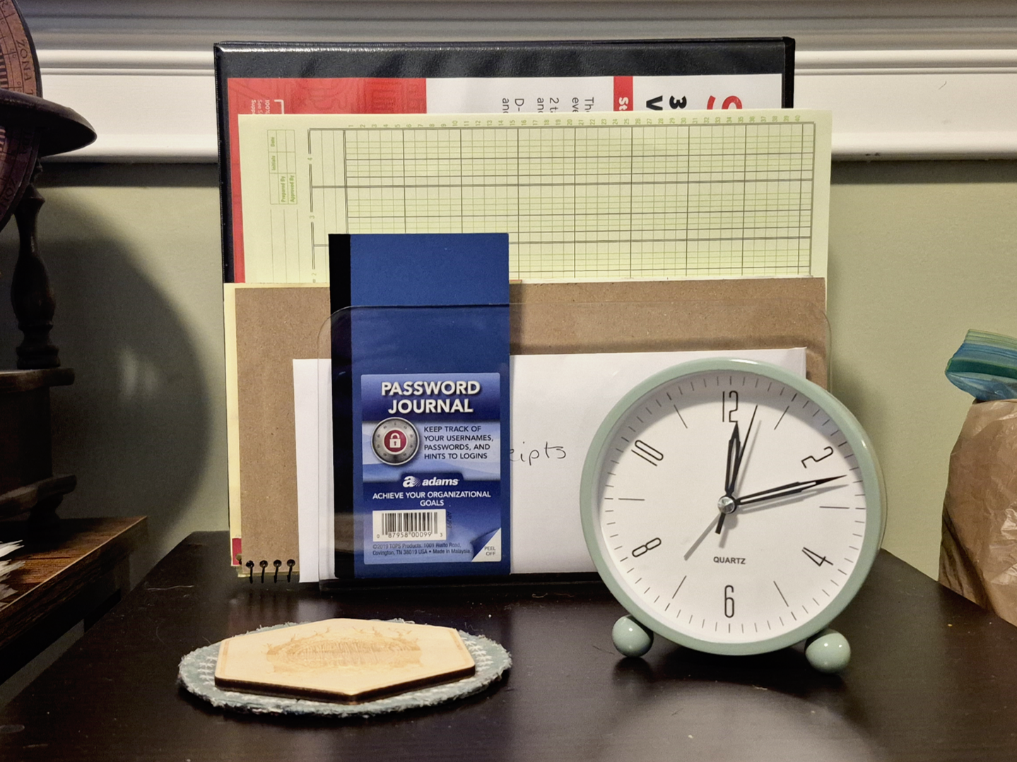 A binder, notepad, and password journal sit in a desk organizer. A coaster to the left and alarm clock to the right sit in front of the desk organizer.