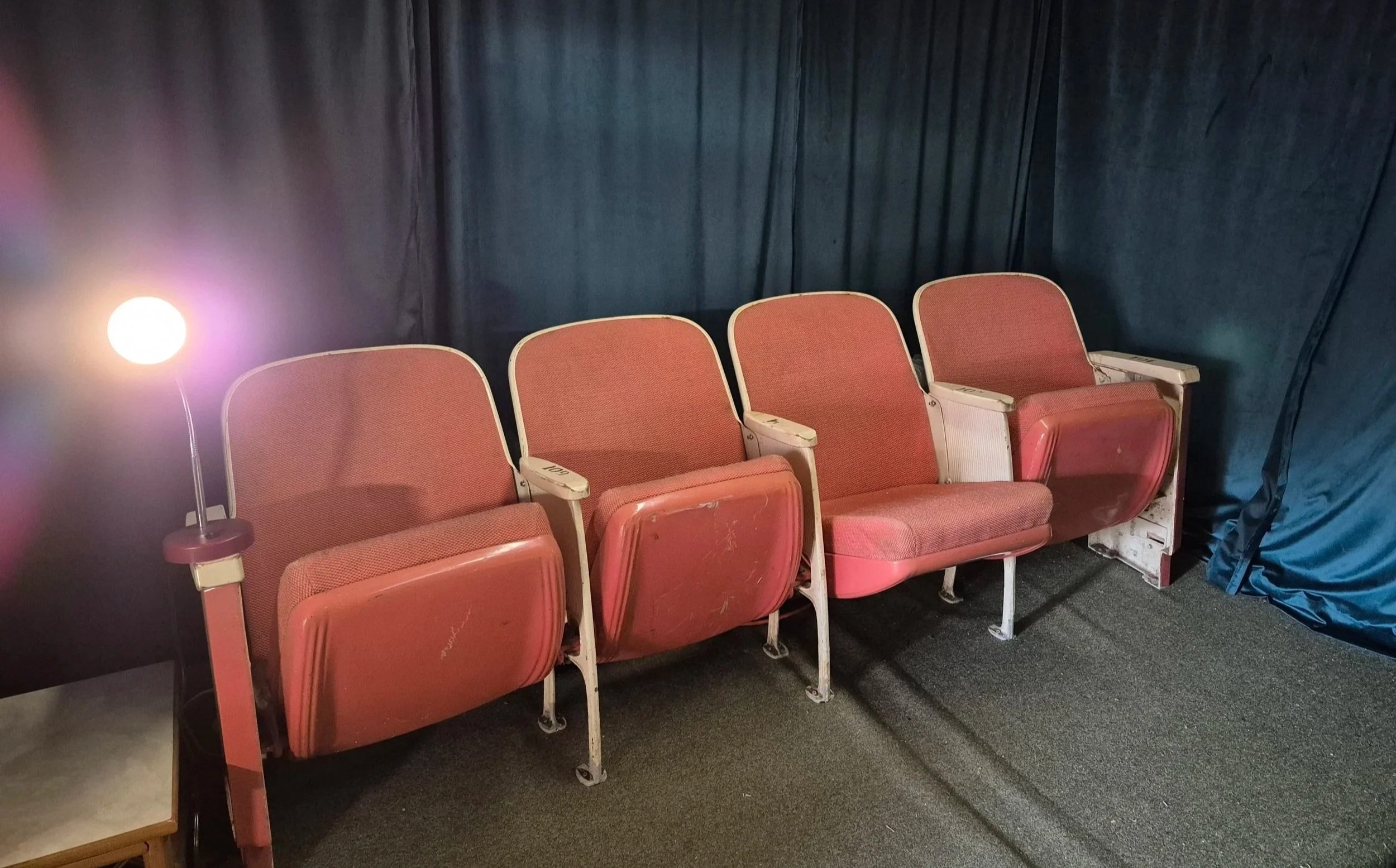 A bright light shines next to a row of coral colored movie theater seats.