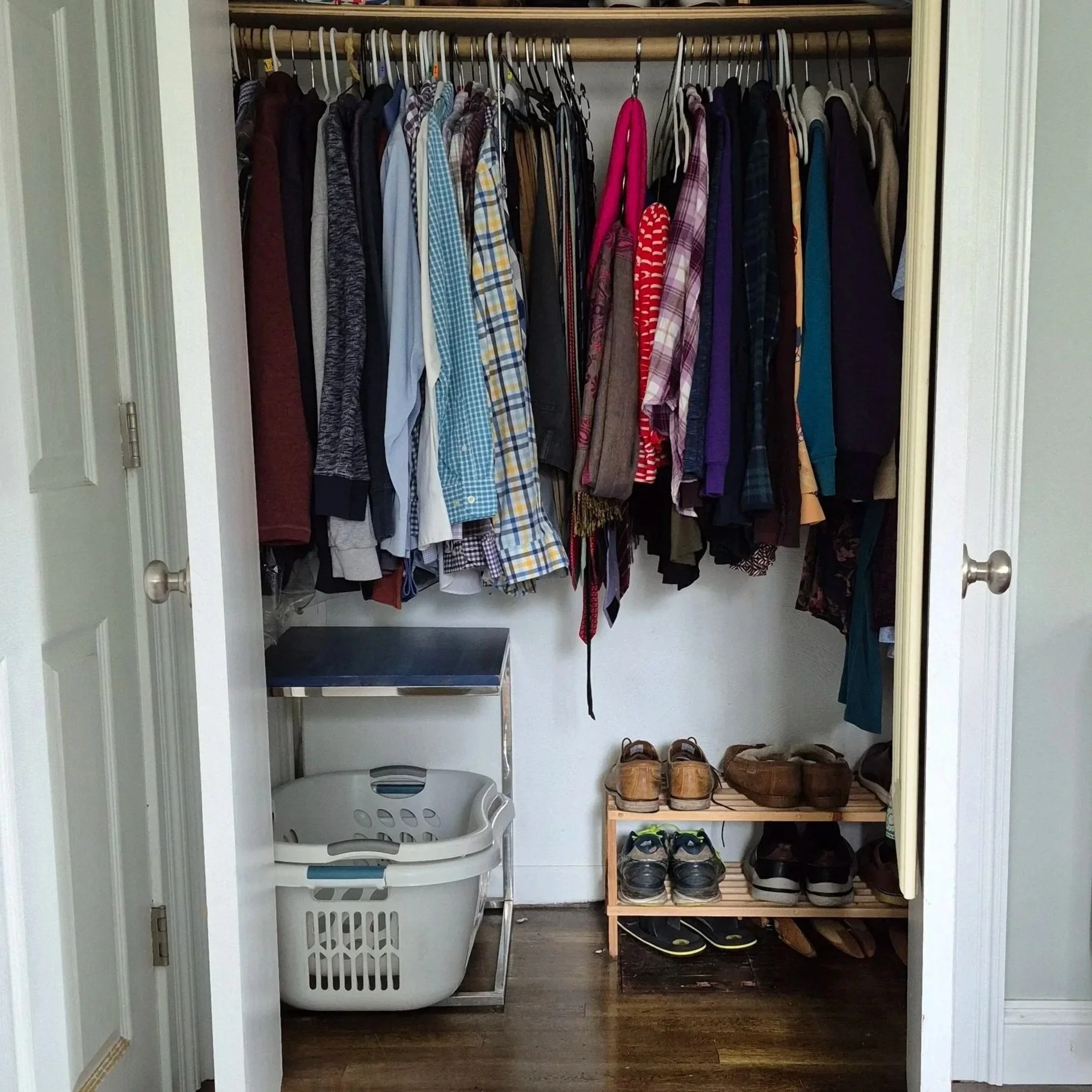 Clothes hang in a closet. Under the clothes sit a laundry basket to the left and a shoe rack to the right.
