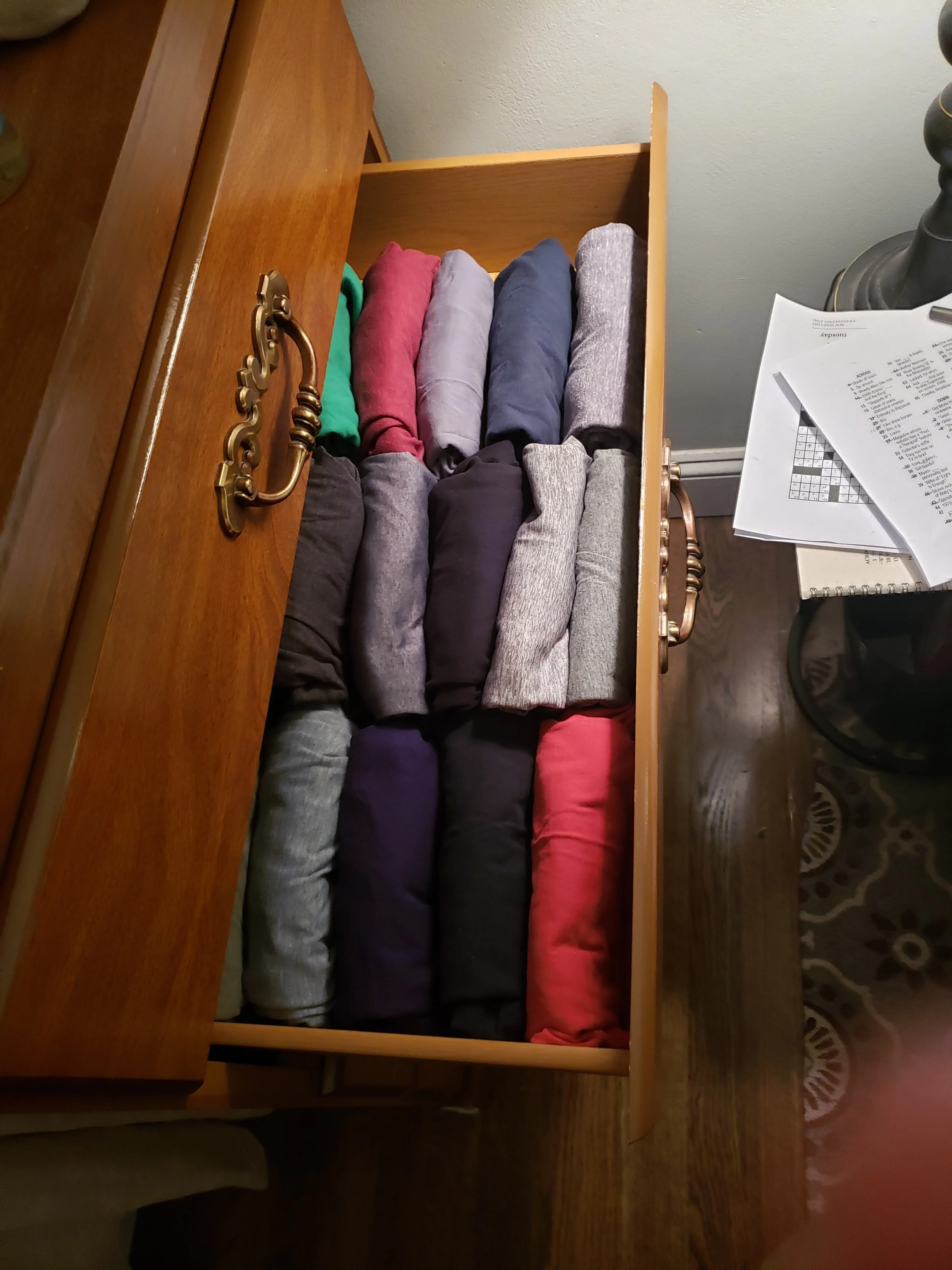 Bird's eye view of tee shirts folded KonMari style in open bureau drawer.