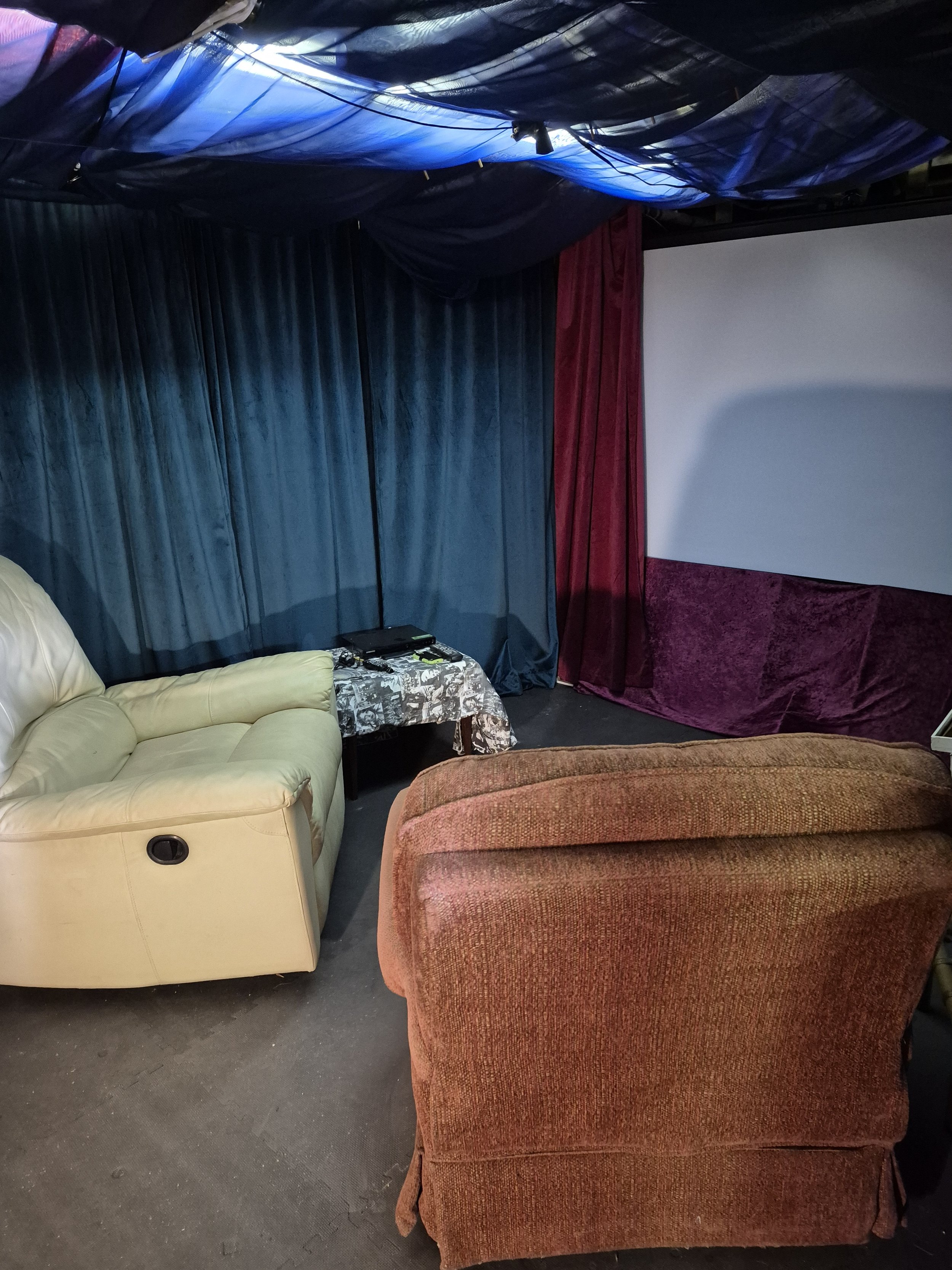 Basement hung with deep green and red curtains draping the walls and ceiling to emulate an old fashioned movie theater. Two easy face a projection screen.