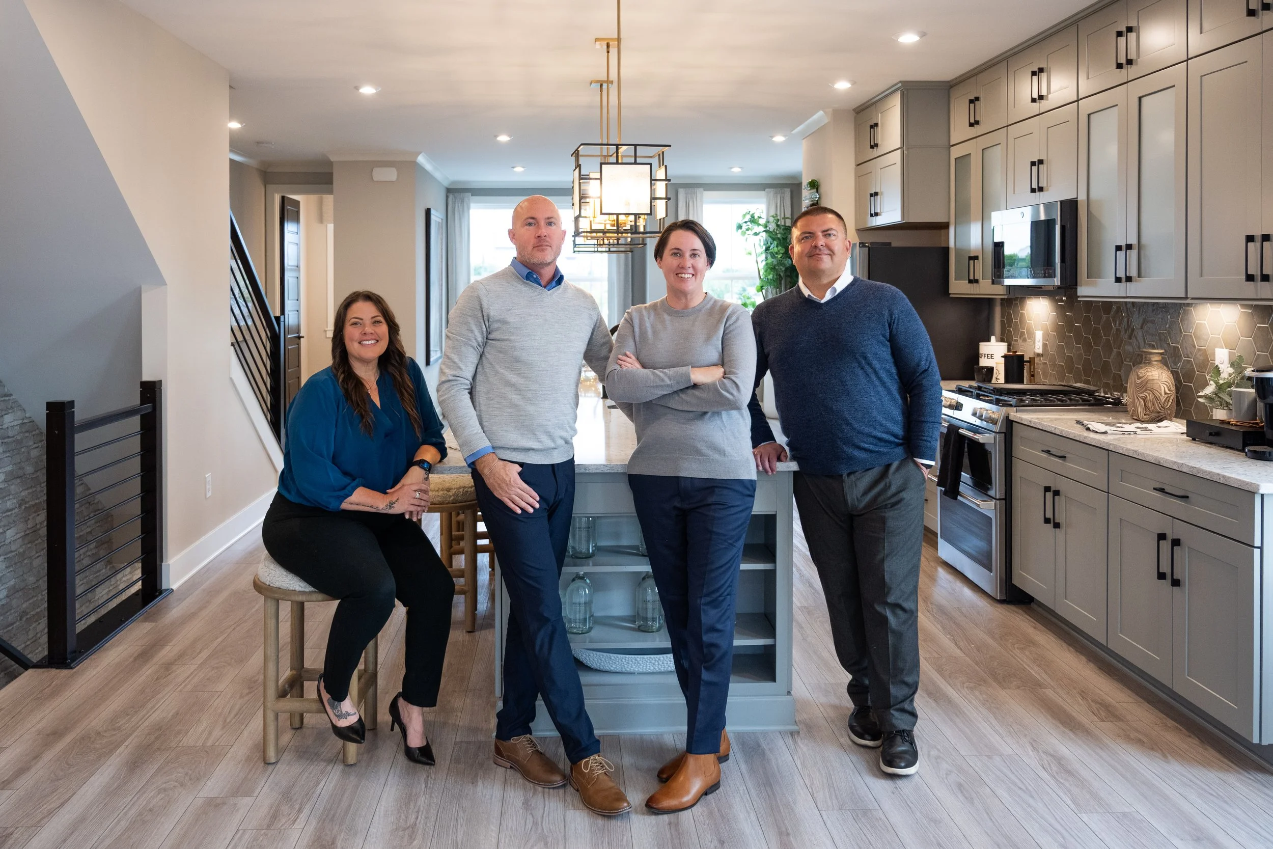 Group of four people posing in a modern kitchen with light-colored cabinets, stainless steel appliances, and a central island.