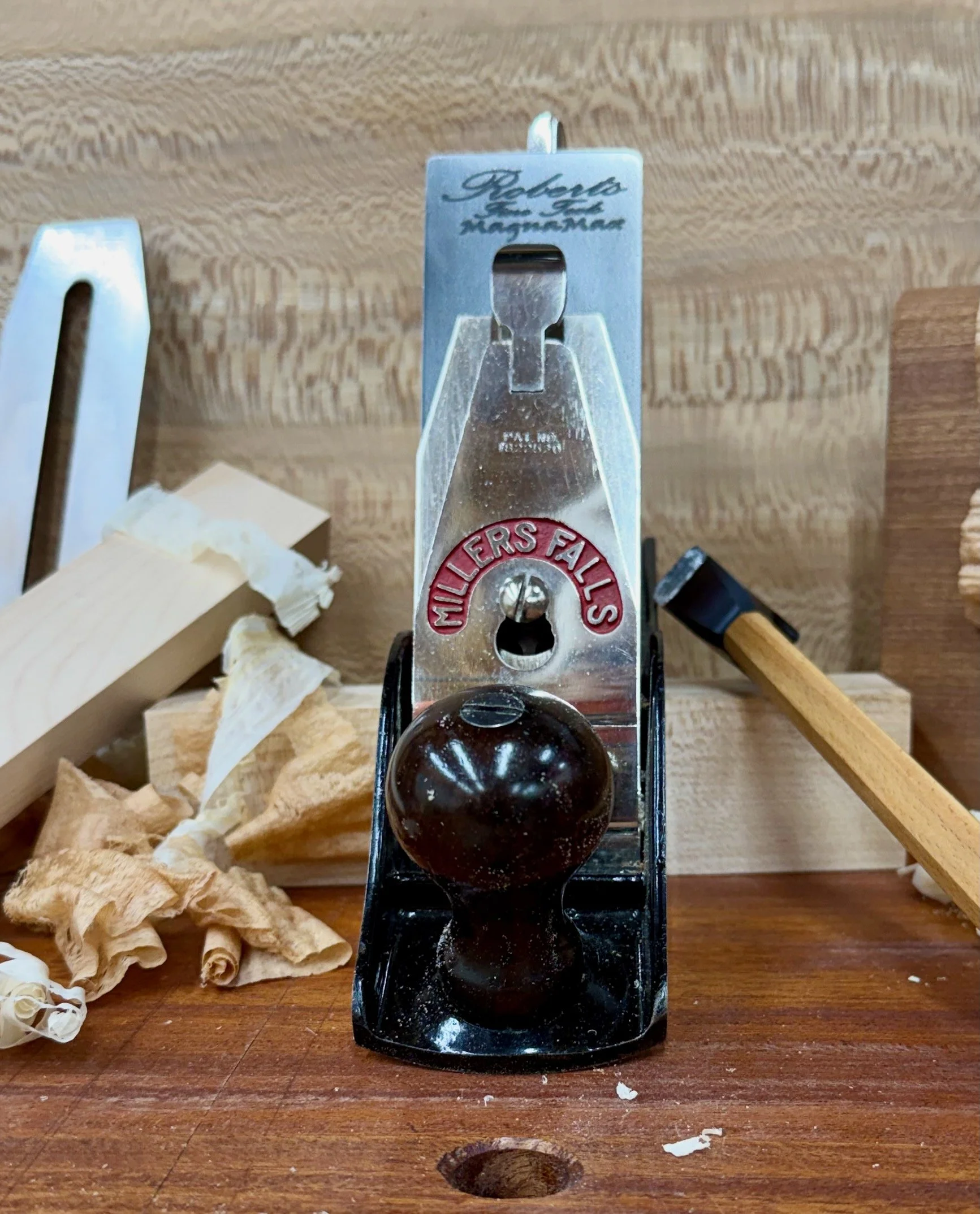 A woodworker's workbench with a hand planer, shavings, and wood pieces.