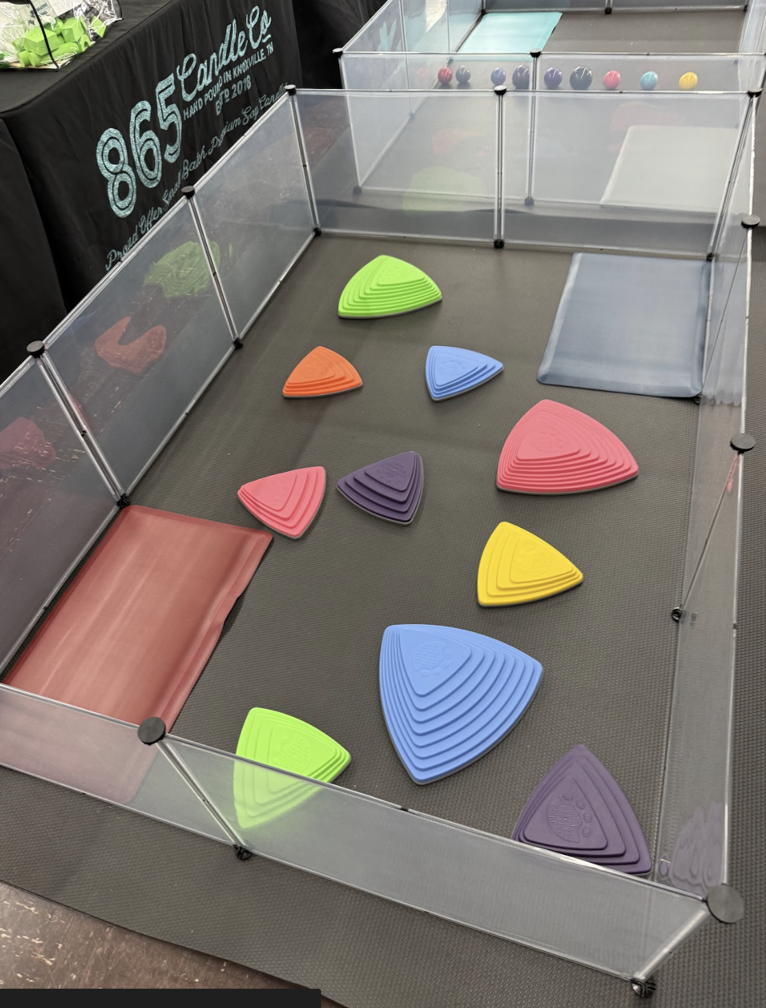 A trampoline with multicolored, triangular-shaped stepping stones inside the bounce area, surrounded by a clear safety enclosure.