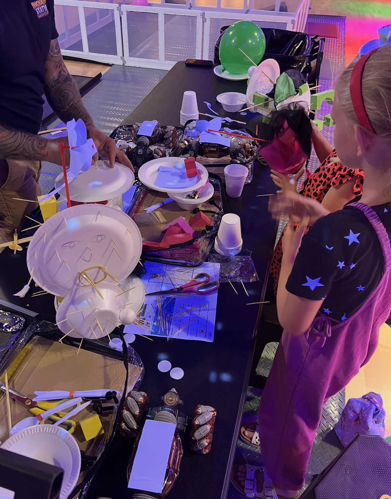 Children's robotics competition with colorful robots and obstacles on a black mat.