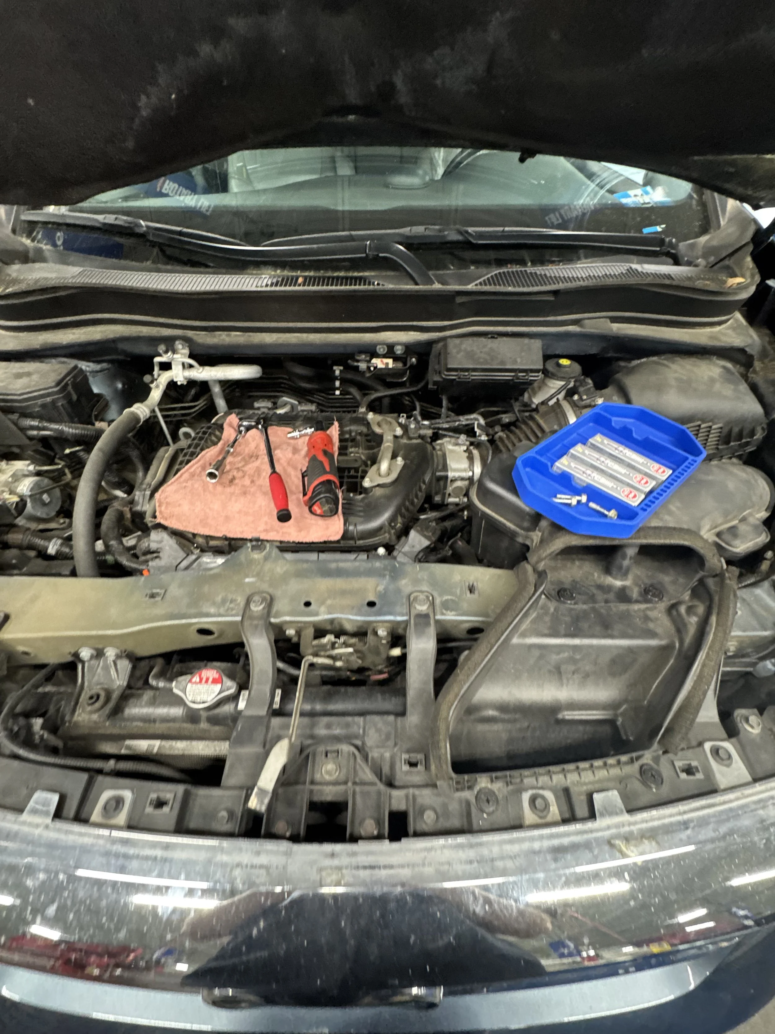 Car engine with tools and a blue container of screws on top of it, in a repair shop or garage.