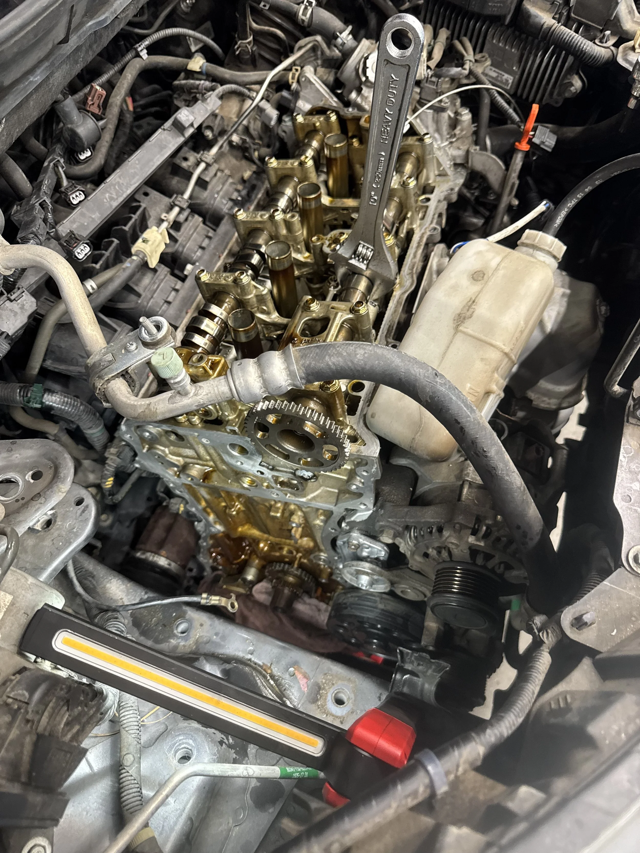 Close-up view of an engine with the valve cover removed, exposing the camshaft, timing gear, and engine components, with some oil on the surface.