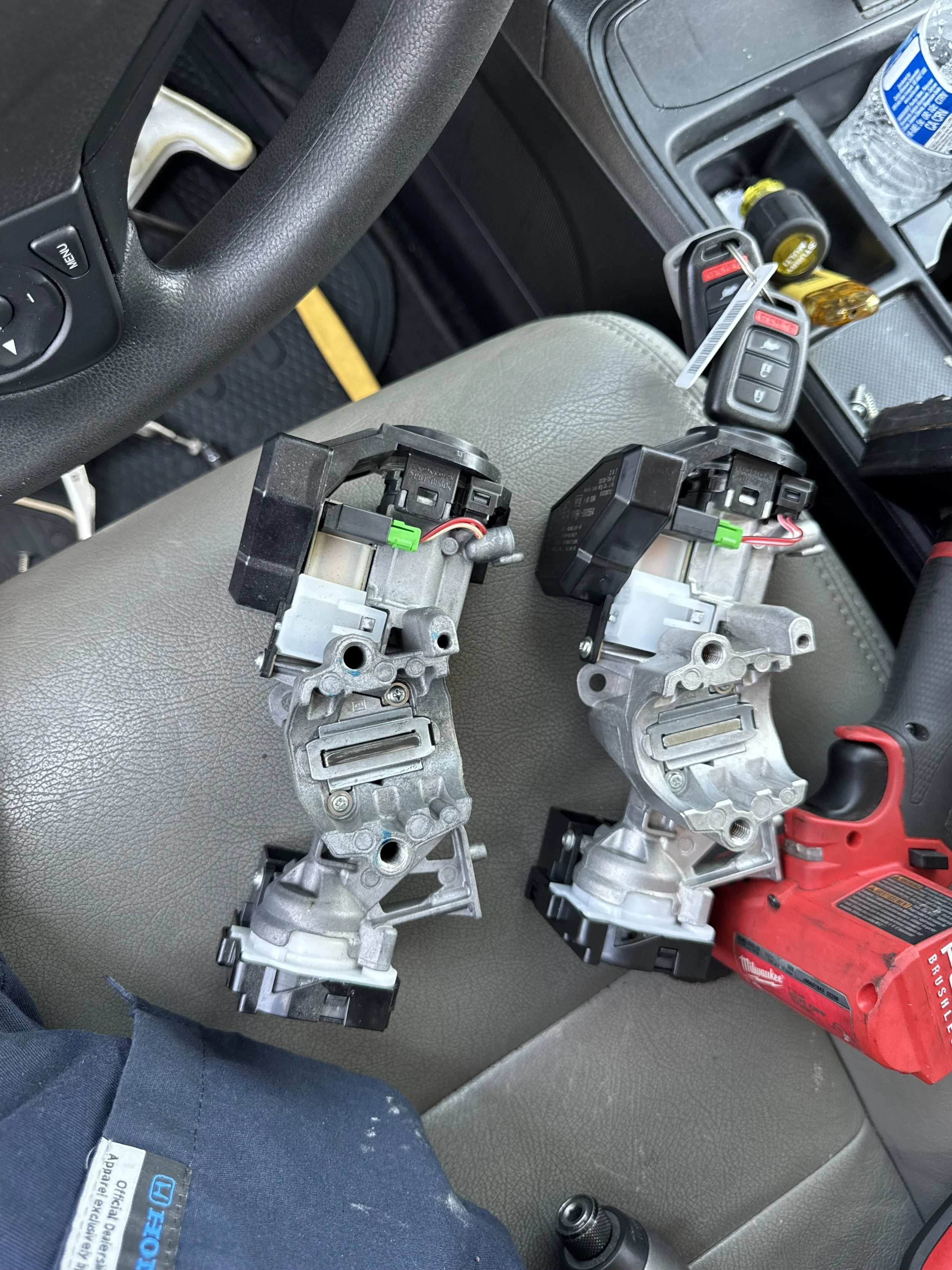 Car interior with two electronic components, a Milwaukee power tool, a key fob, a water bottle, and various small items on the center console.