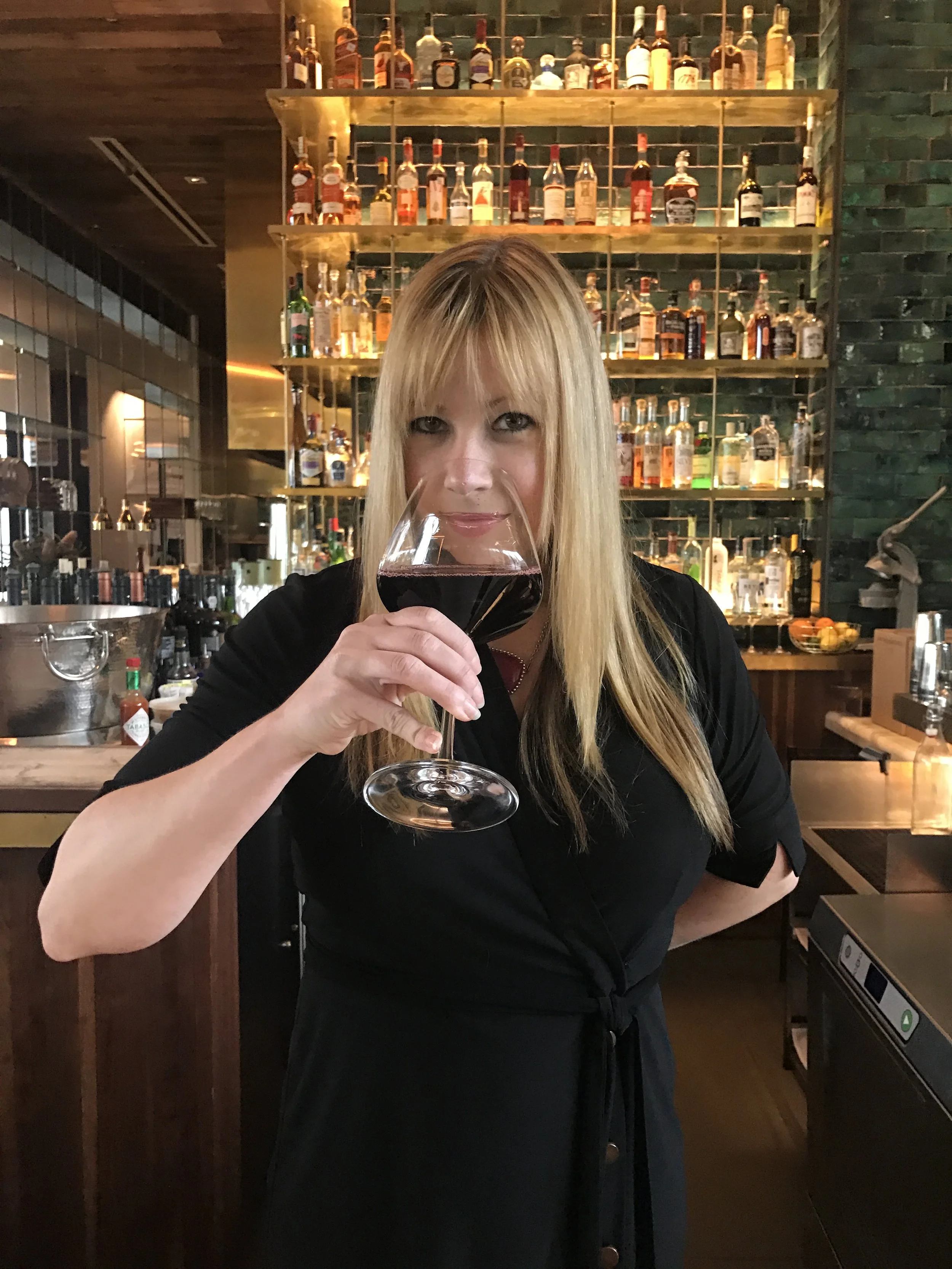 Woman with blonde hair holding a glass of red wine in a bar setting.