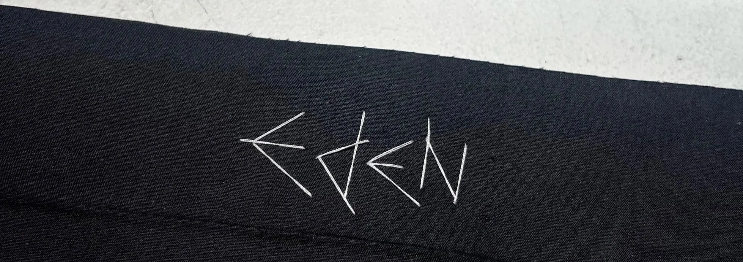 Close-up of black fabric with a logo or name embroidered in white thread.