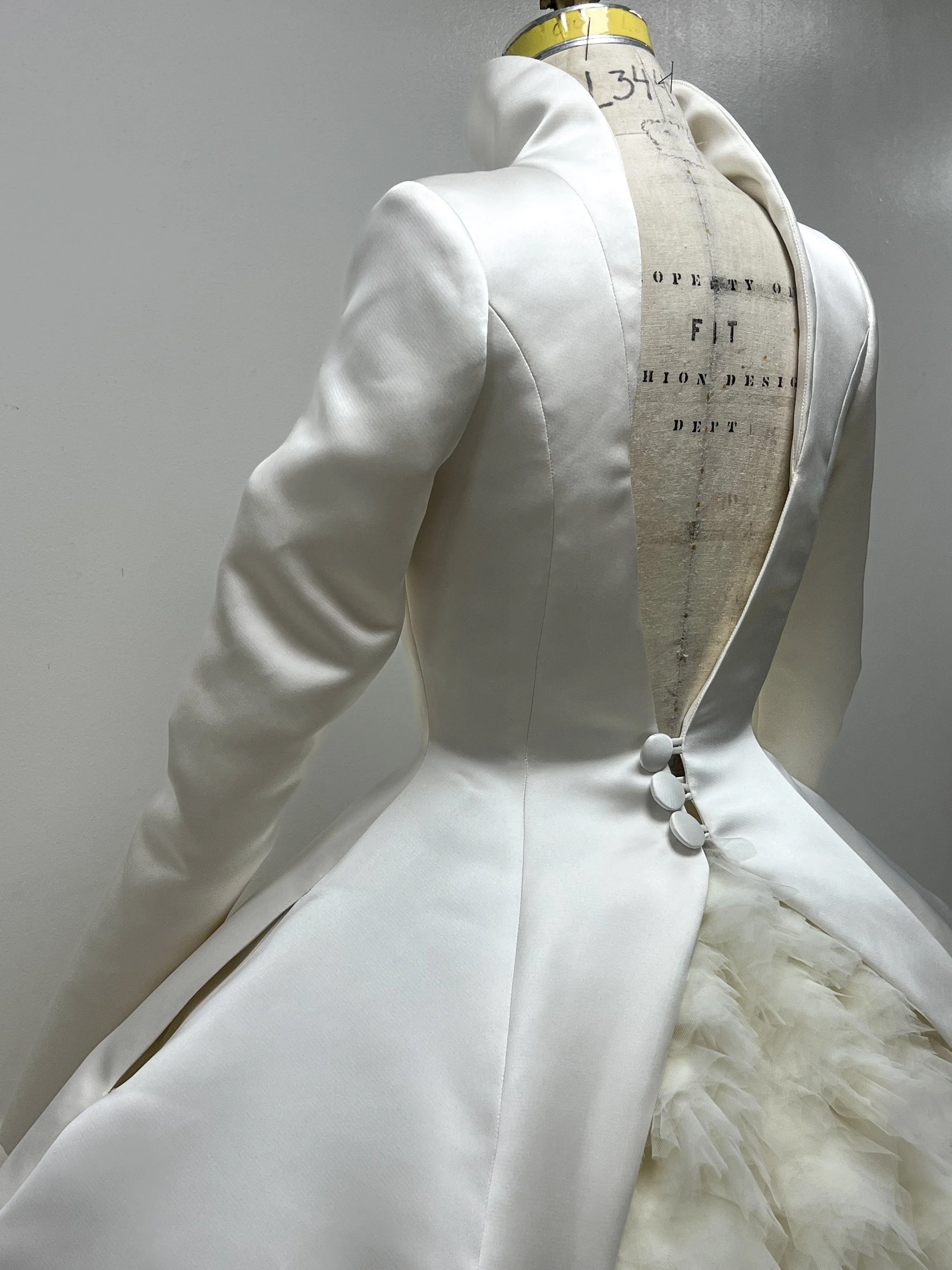 A white evening gown on a dress form with a feathered train, satin fabric, and button details on the back.