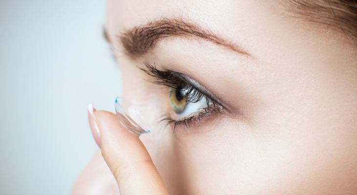 Close-up of a person inserting a contact lens into their eye.