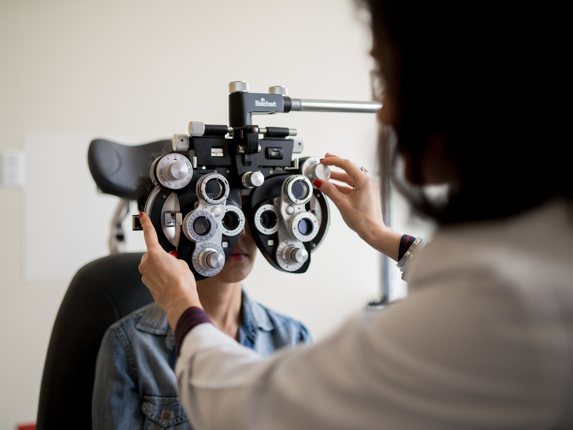 A woman getting an eye exam with a phoropter during an eye assessment in an optometrist's office.