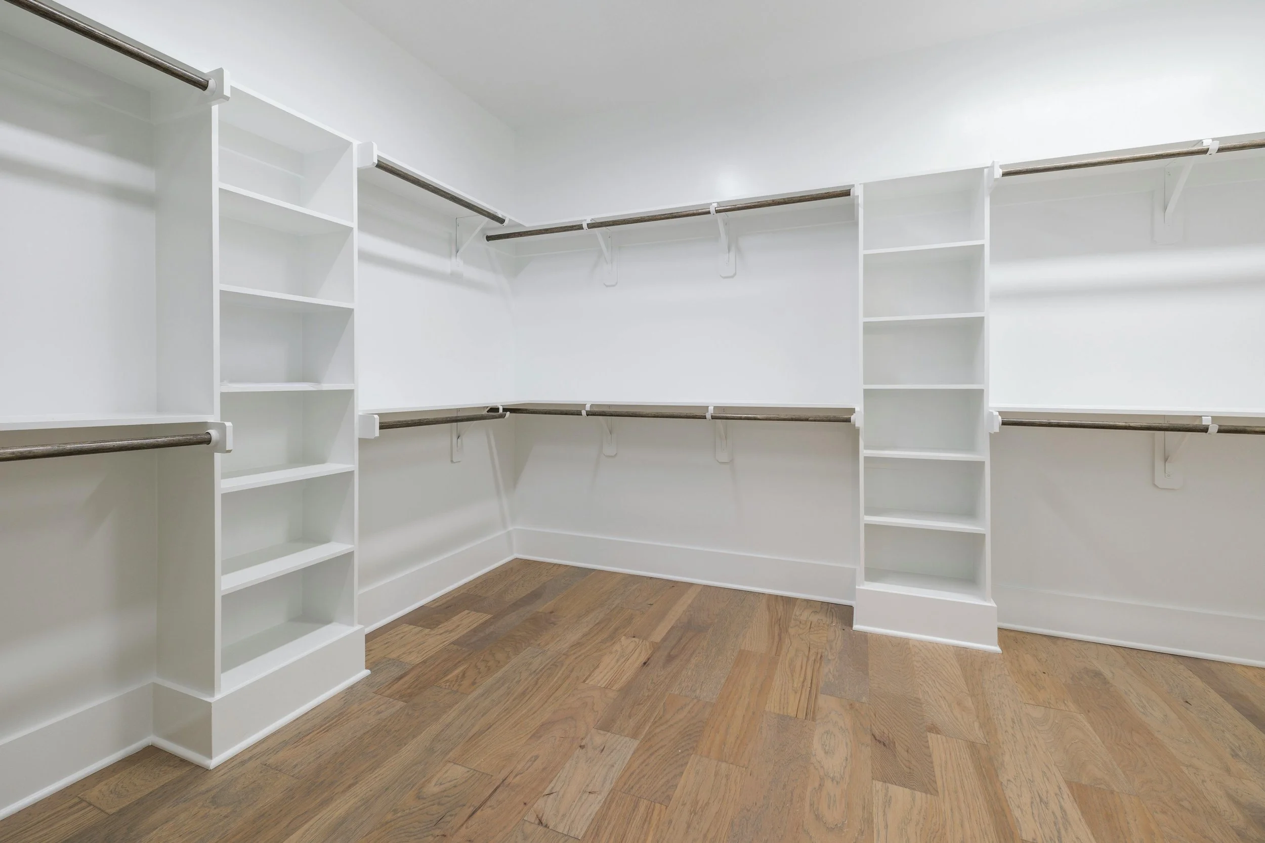 Empty walk-in closet with white walls, built-in shelves, and wooden flooring.
