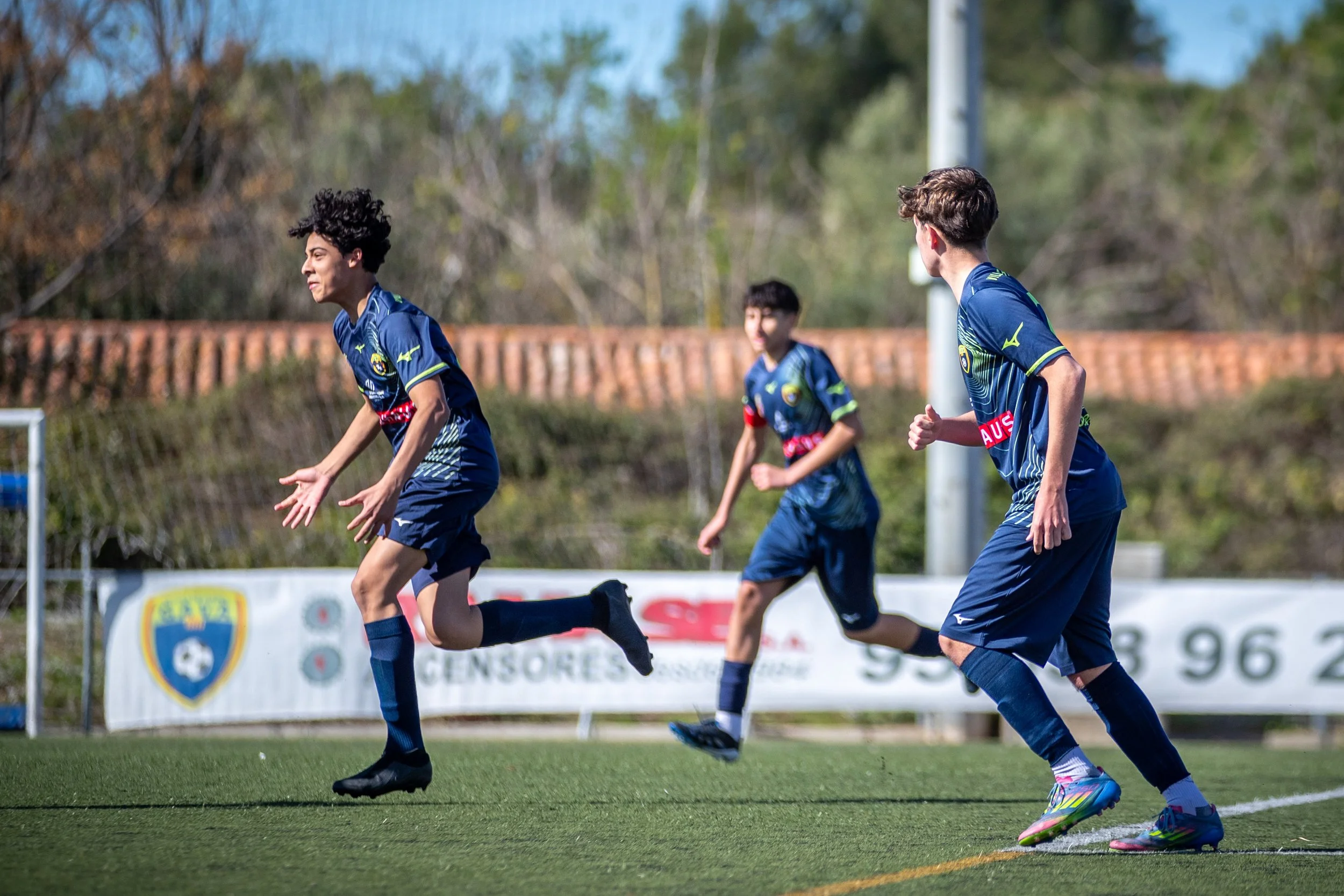 Three soccer players in blue uniforms running on the field during a game.