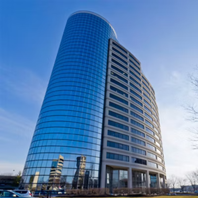 A modern, blue glass office building with curved architectural design and multiple floors, set against a clear sky.