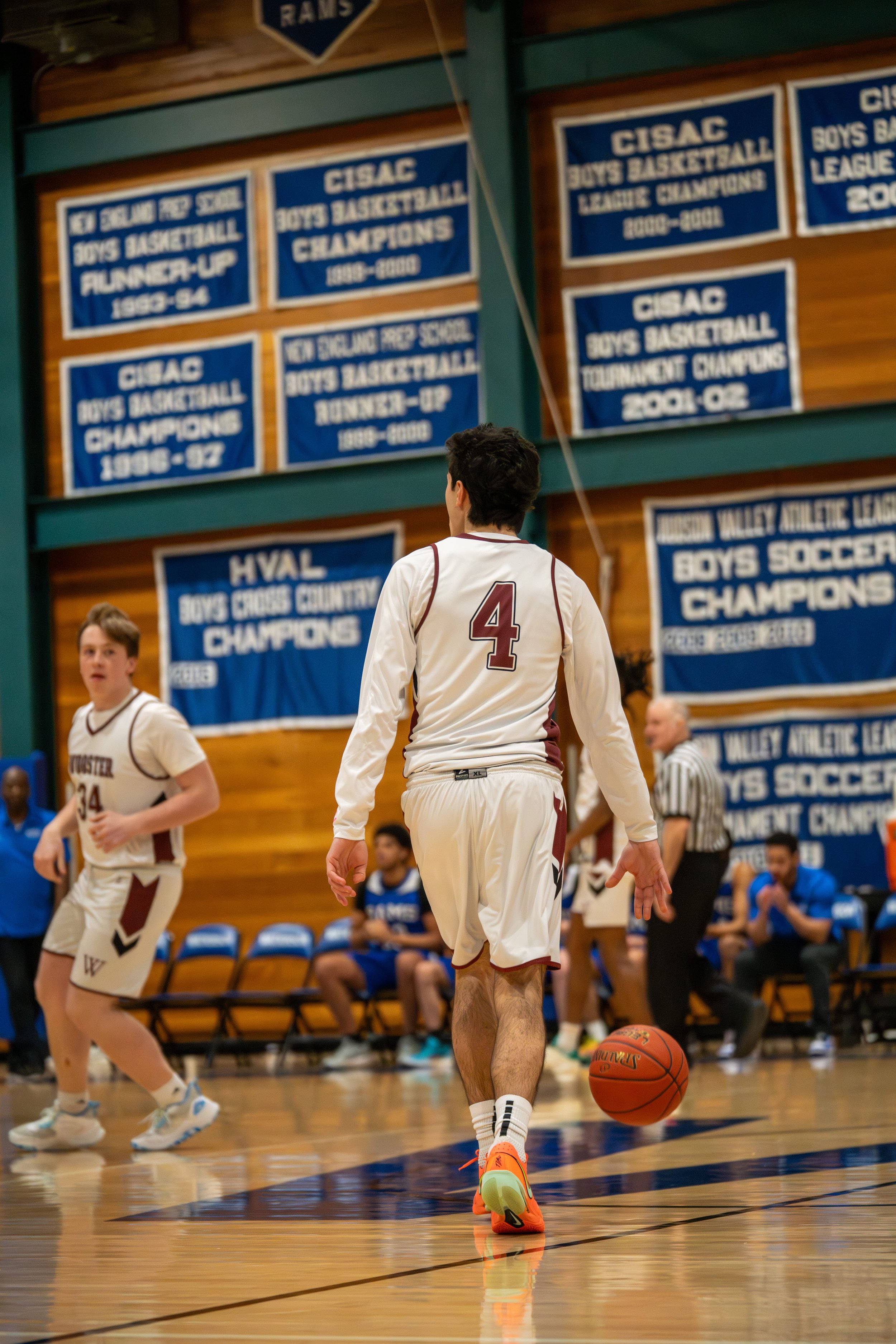 A basketball player wearing a white jersey with the number 4, dribbling a basketball on an indoor basketball court during a game.