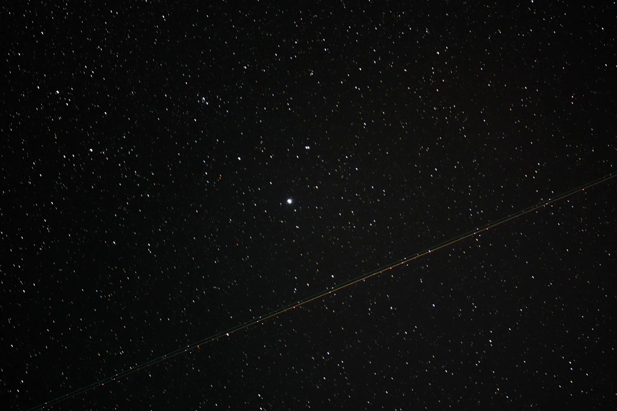 Night sky filled with stars and a faint streak from a passing satellite or satellite trail.