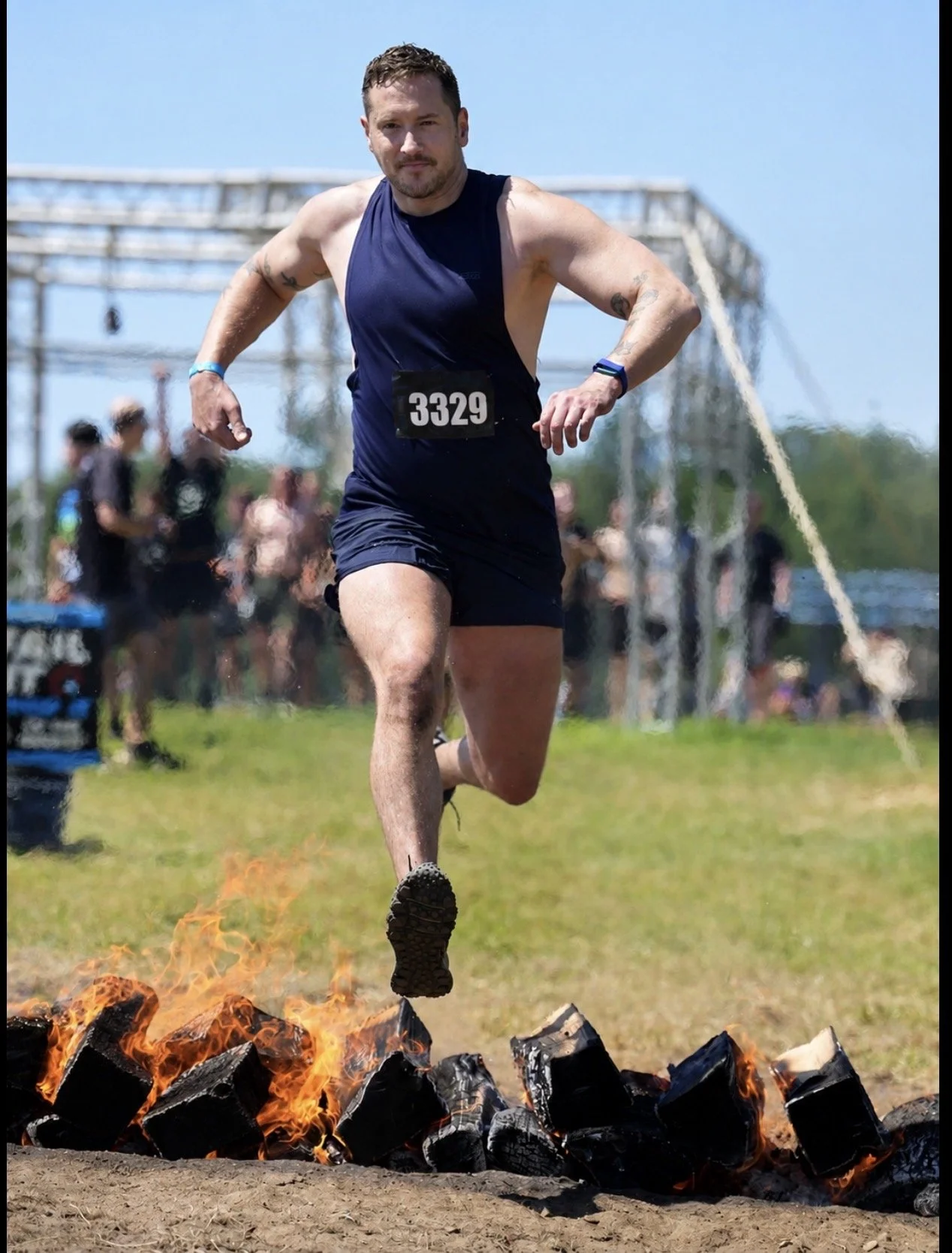 Man running over a fire with rocks and flames, participating in an outdoor event, wearing a bib number 3329, and dressed in athletic clothing.