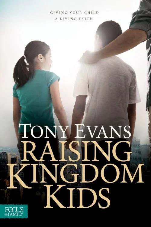 Back view of a man and two children, a girl and a boy, standing outdoors with a city skyline in the background. The man has his arm around the boy's shoulder, and they all face away from the camera.