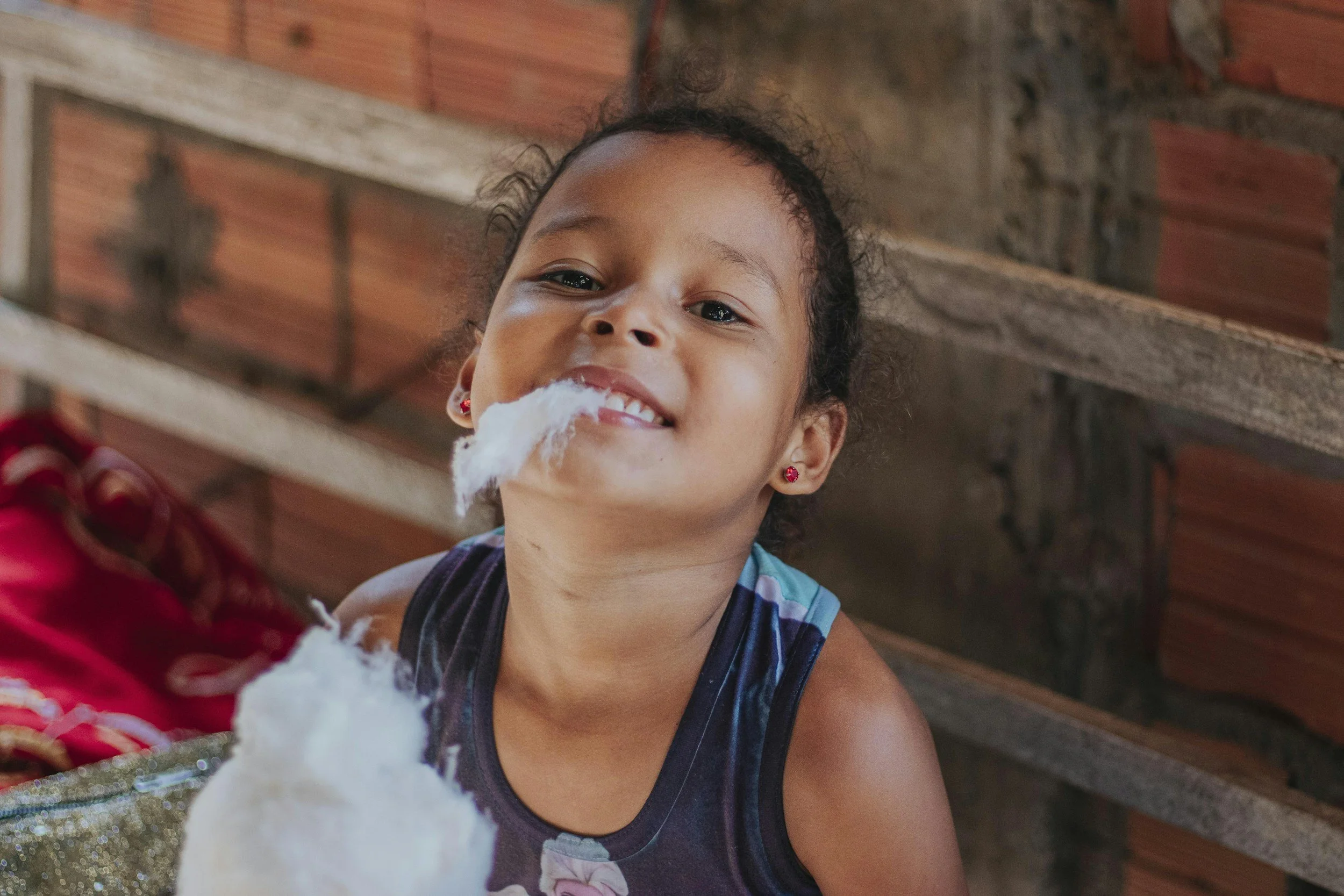 A young girl smiling with cotton candy in front of a brick wall.