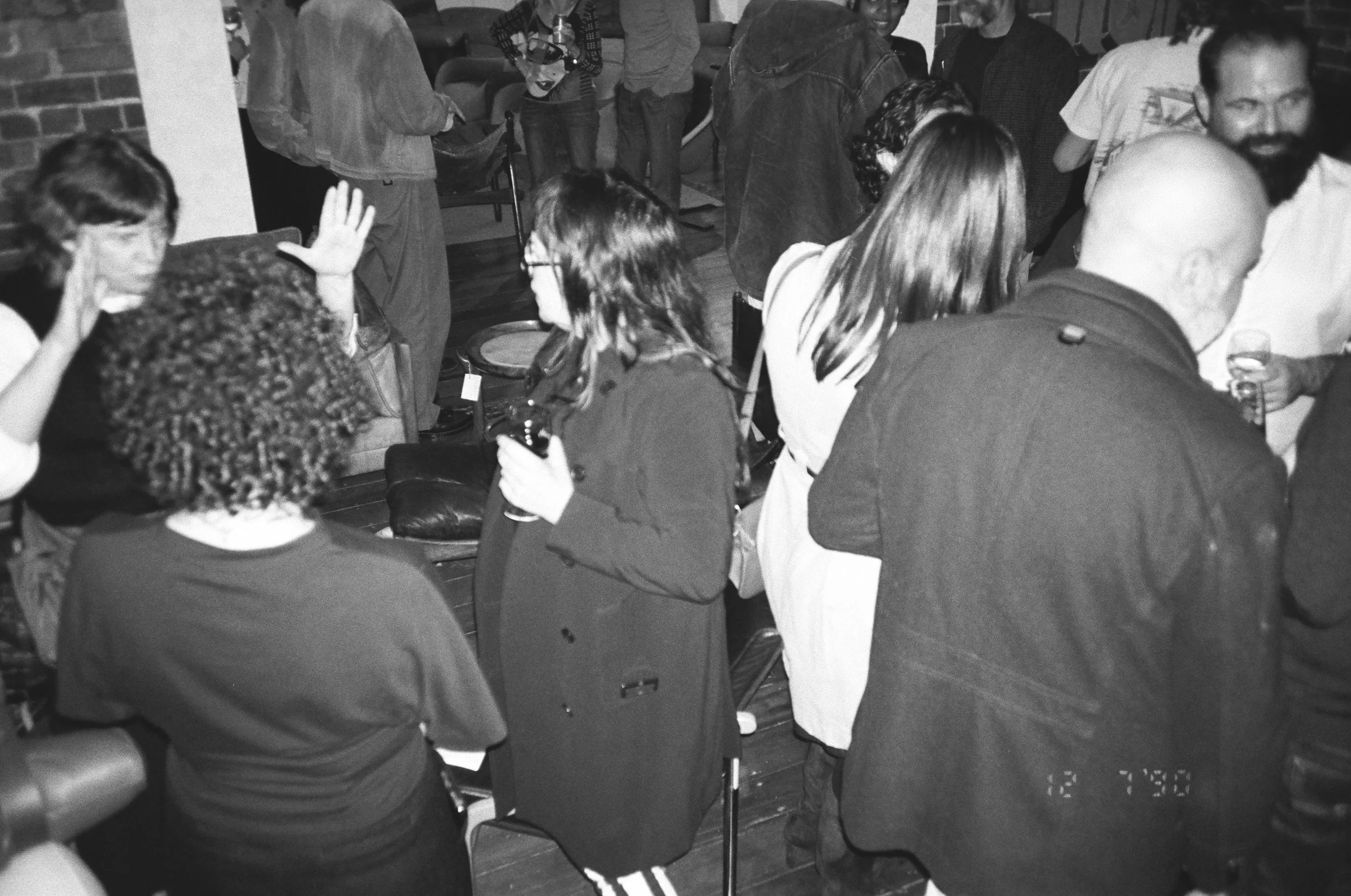 A group of people gathered in a room, some sitting and some standing, engaging in conversation during a social event.