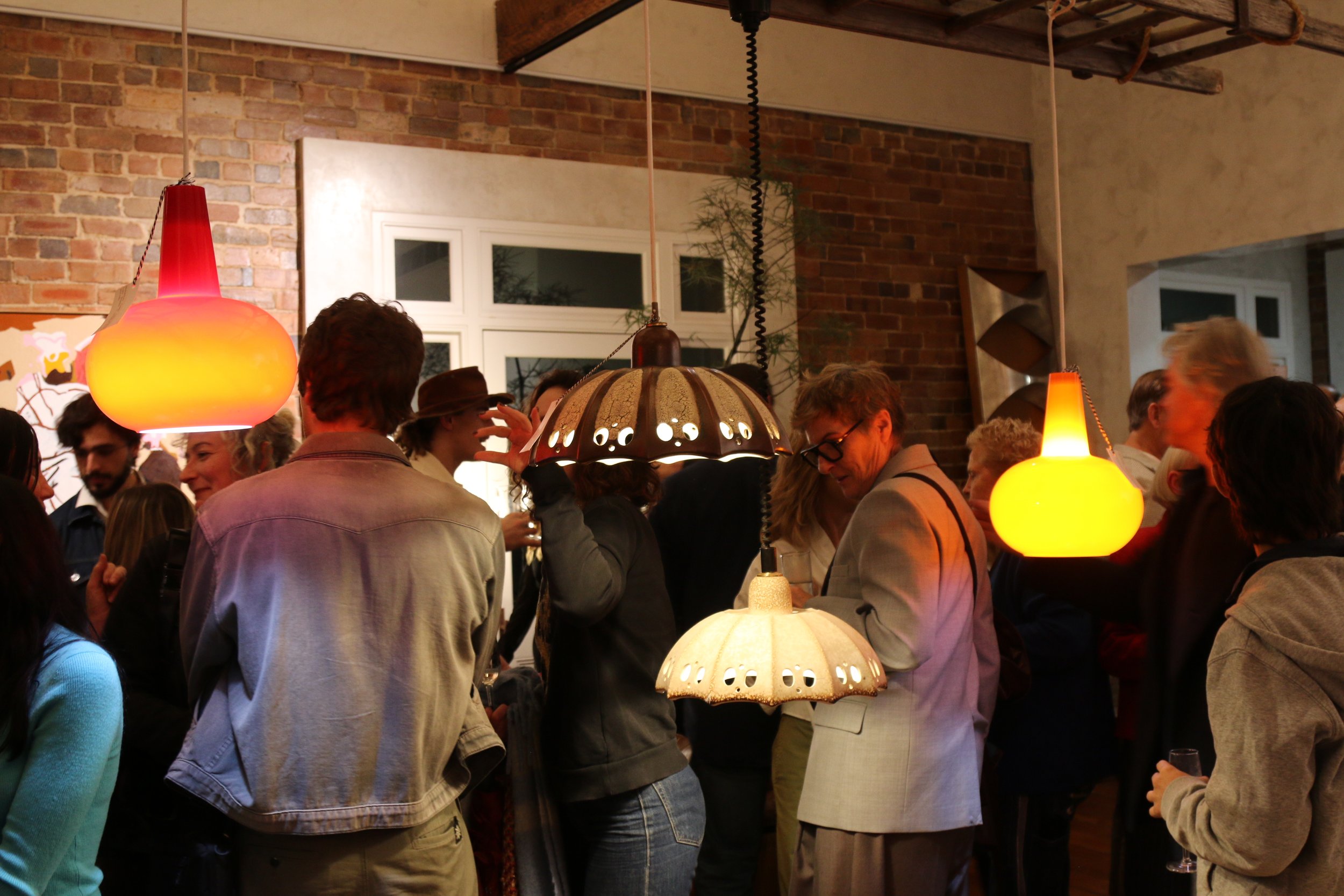 People gathered at a social event in a warmly lit indoor space with hanging lamps and brick walls.