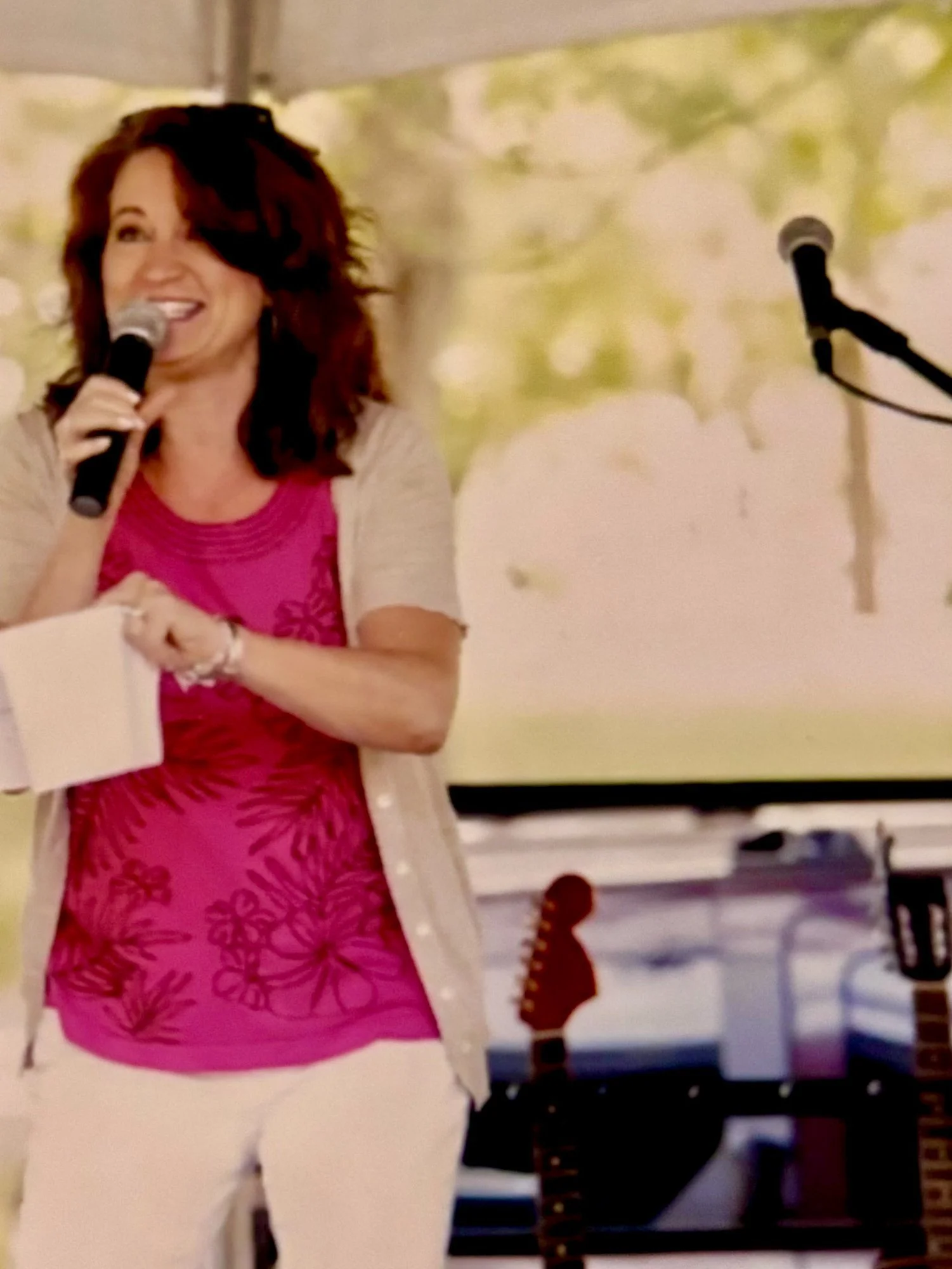 Woman smiling, holding a microphone, standing in front of a colorful background with animal silhouettes.
