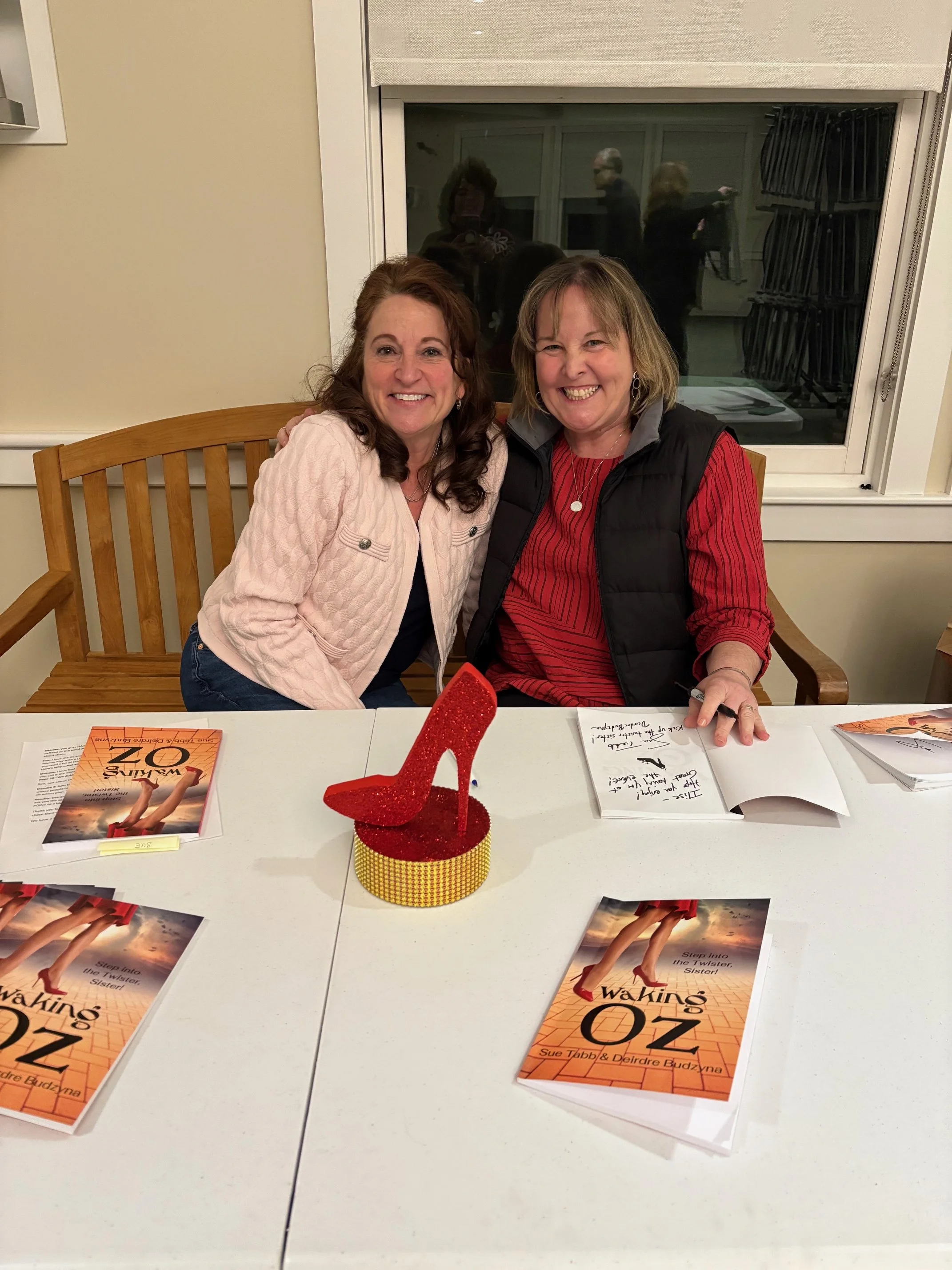 Two women sitting at a table with copies of the book 'Walking Oz' and a red glittery high-heeled shoe decoration on it.