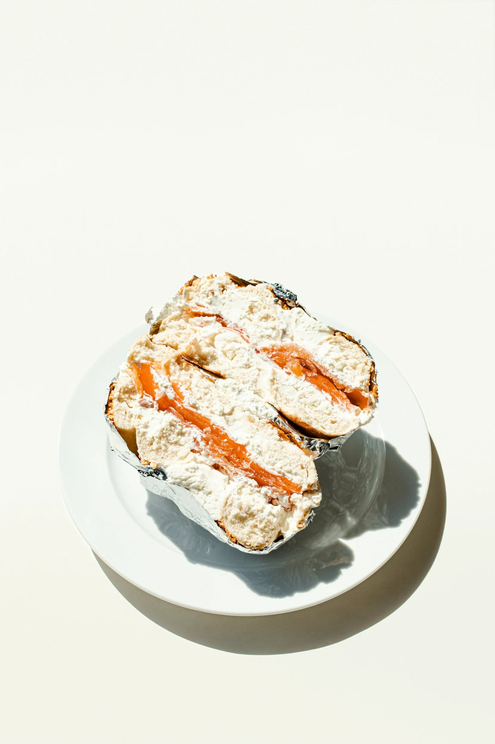 A partially cut piece of cake on a white plate, showing white cream and orange filling, wrapped in silver foil.